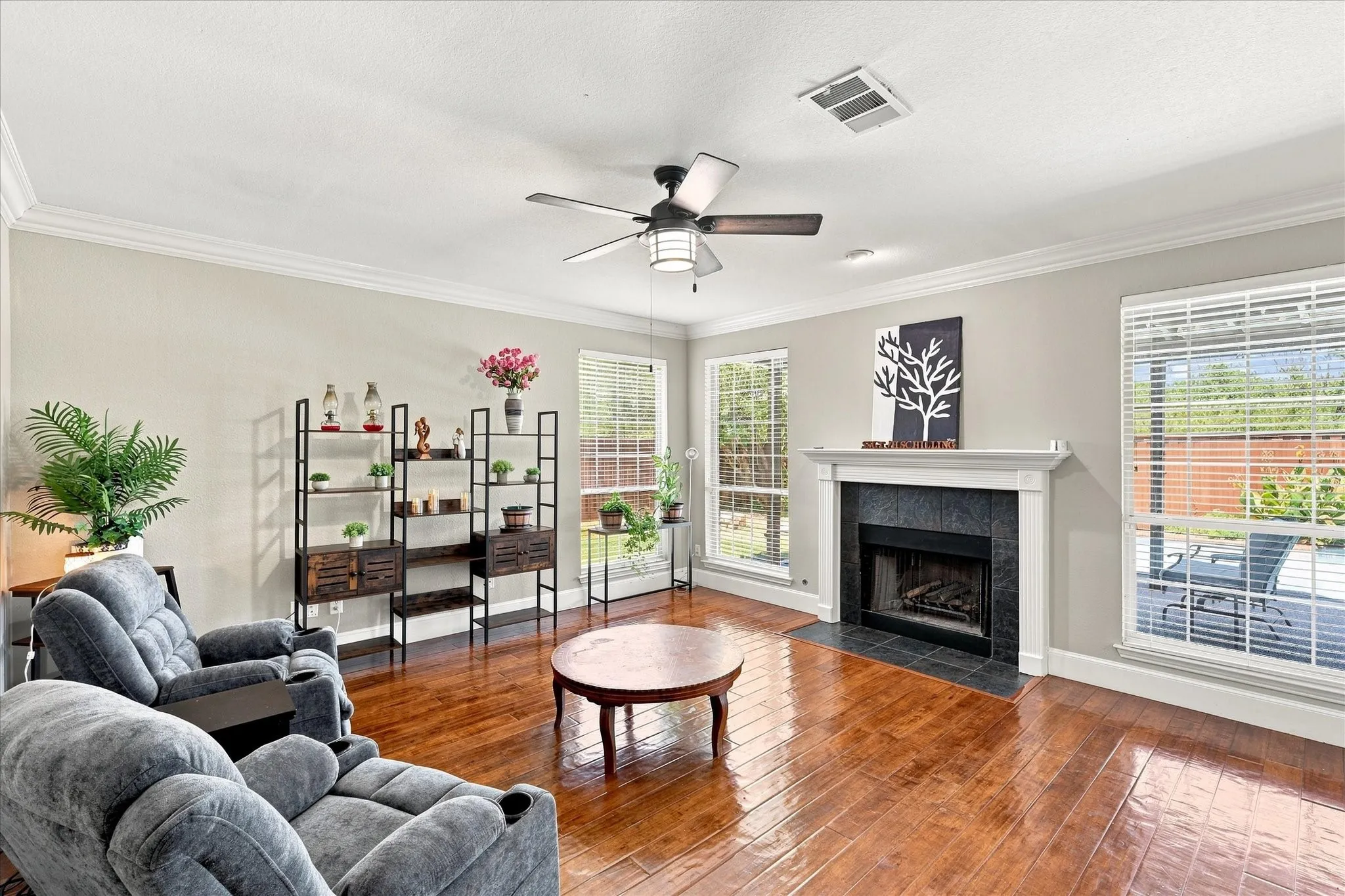 Hardwood-finish flooring, a ceiling fan, crown molding, and a fireplace with a dark tile surround and white mantel