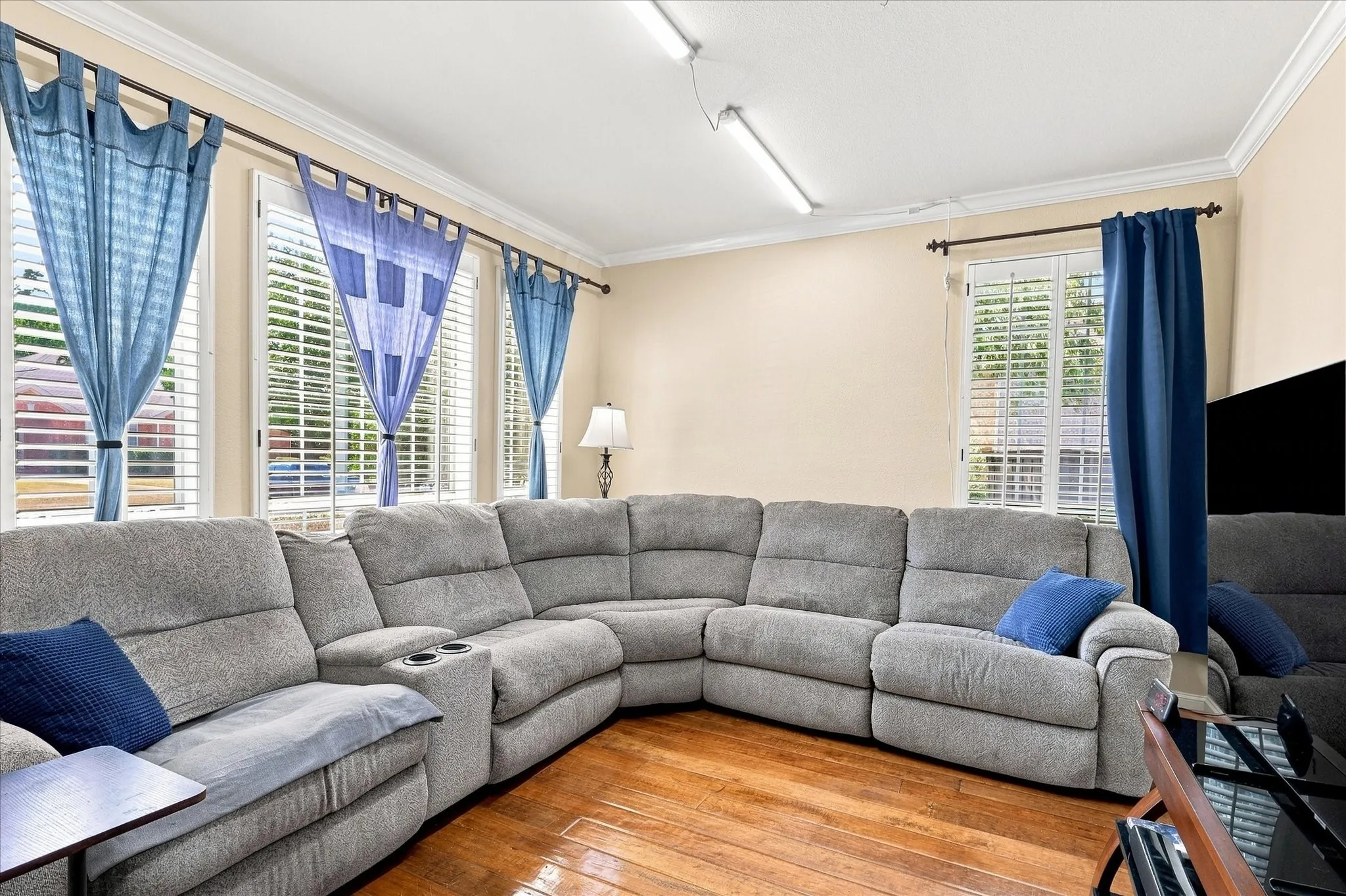 Warm wood-finish flooring with multiple windows featuring plantation shutters, neutral-toned walls, and crown molding