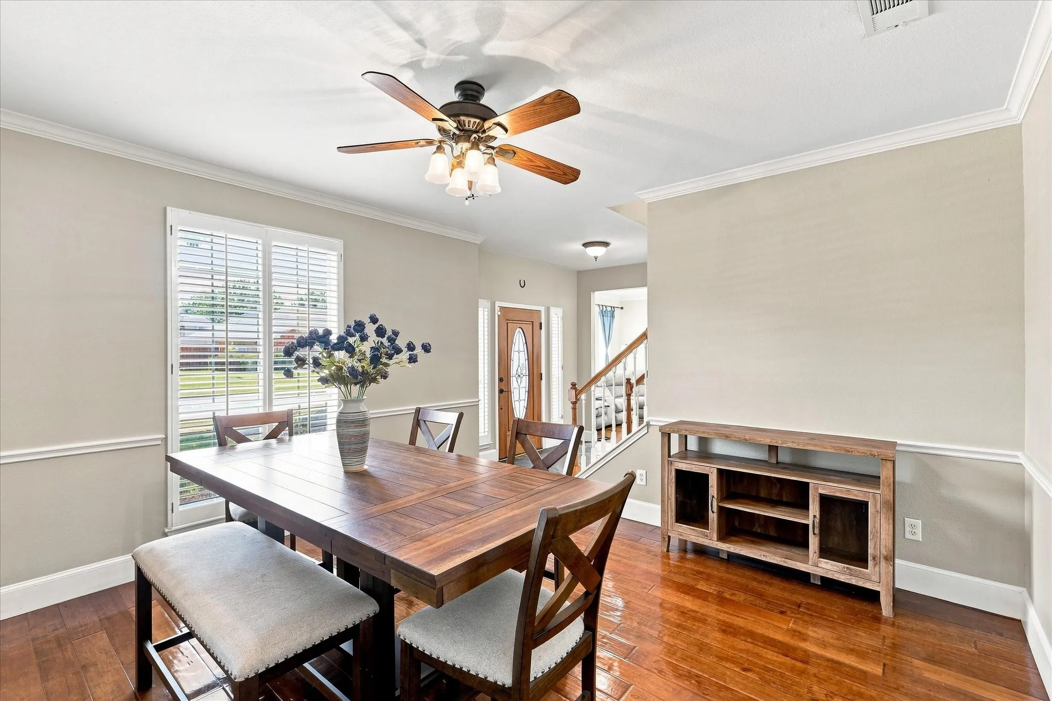 Hardwood flooring, crown molding, chair rail, window with plantation shutters, and a ceiling fan with integrated lighting