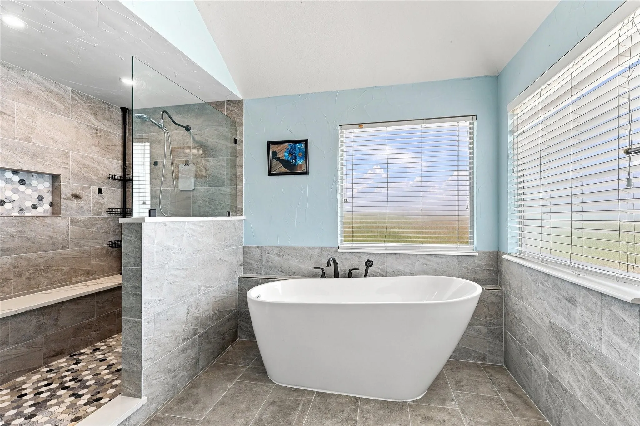 Freestanding soaking tub with floor-mounted fixtures, tiled walk-in shower with a built-in bench, glass shower enclosure, and mosaic tile shower pan