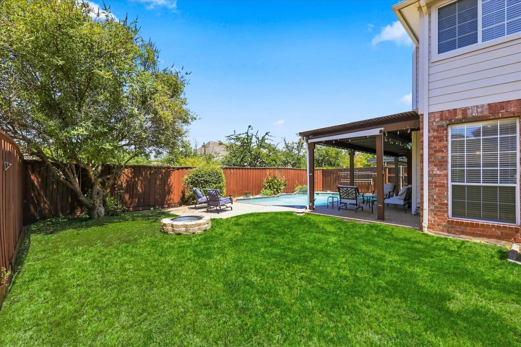Private backyard with a swimming pool, covered patio, stone-surround fire pit, and wood fencing