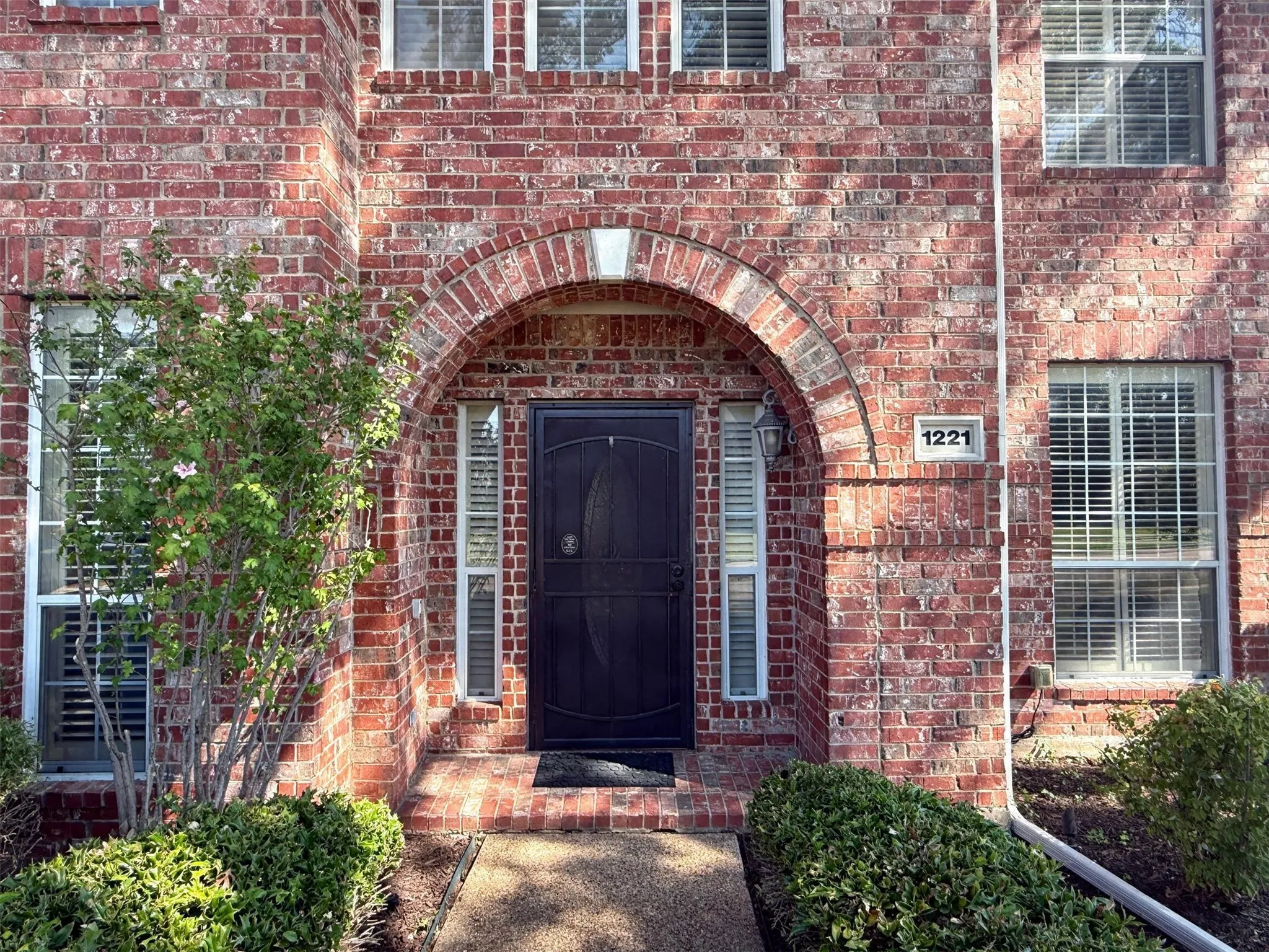 Brick facade with an arched entry, a dark-toned front door, and multiple windows with interior blinds