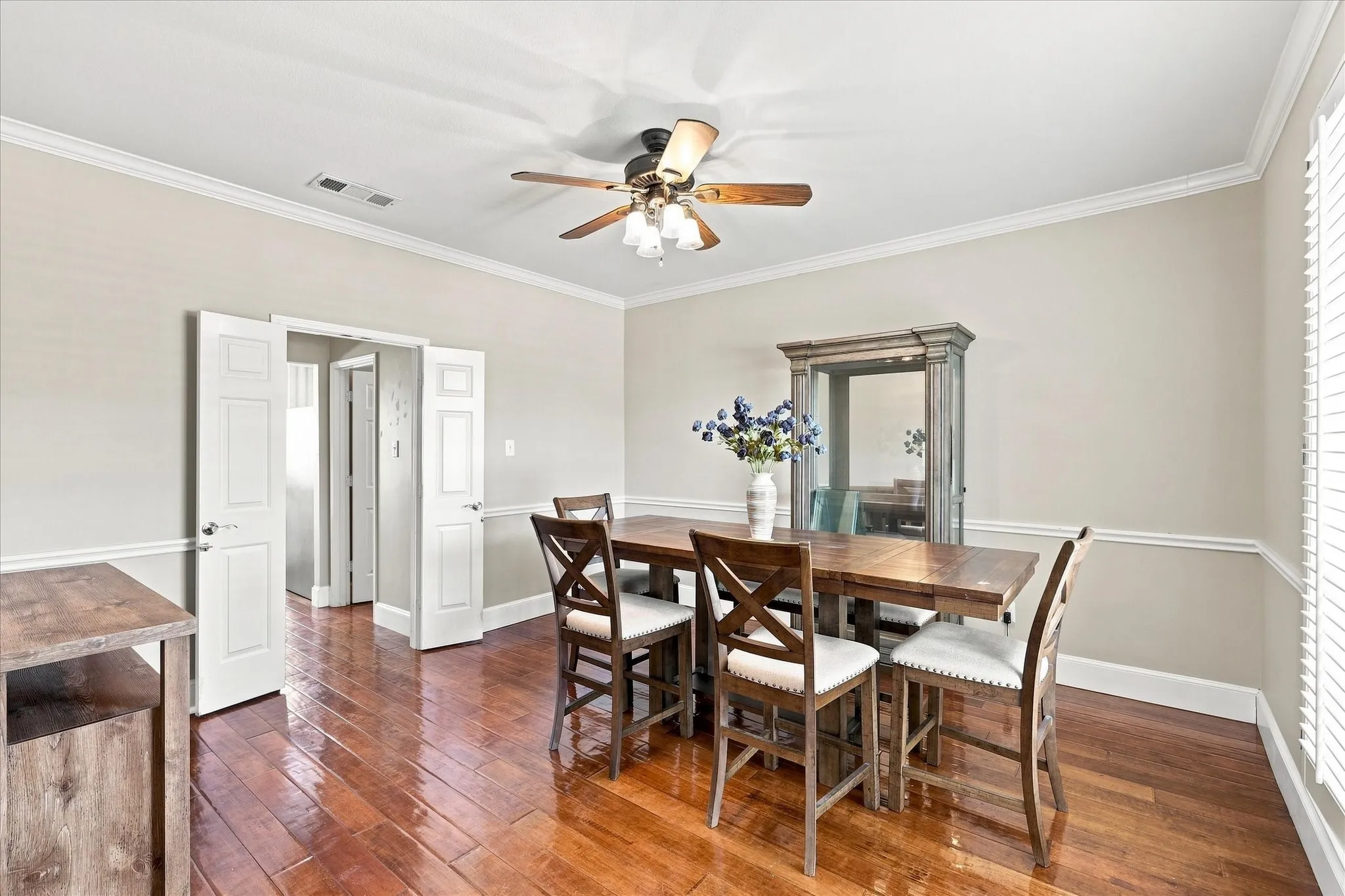 Rich wood-finish flooring, crisp white crown molding, and a ceiling fan with integrated lighting