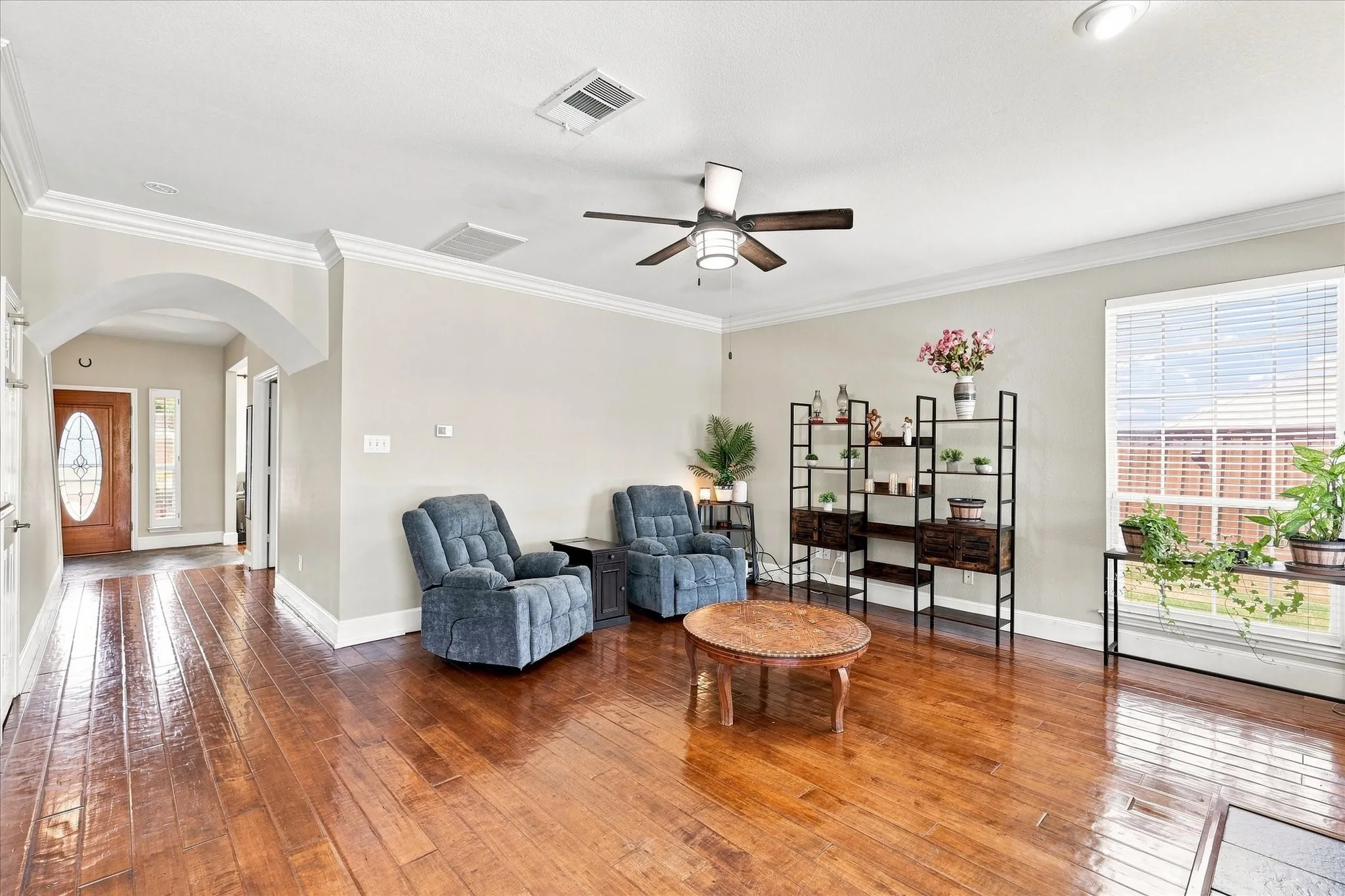 Hardwood-finish flooring, crown molding, arched doorway, ceiling fan, and large window with blinds