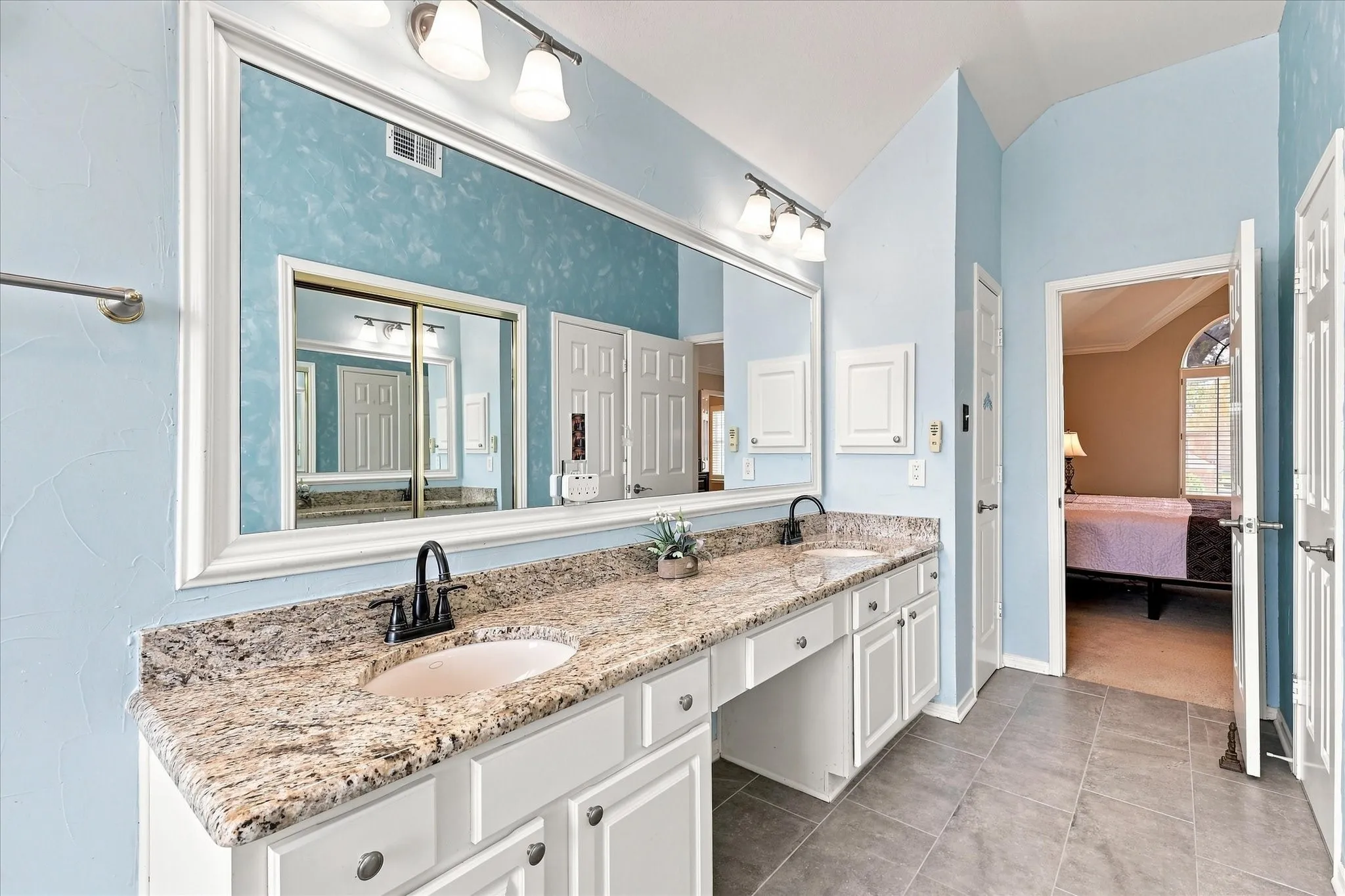 Dual sink vanity with granite countertop, white cabinetry, and tile flooring