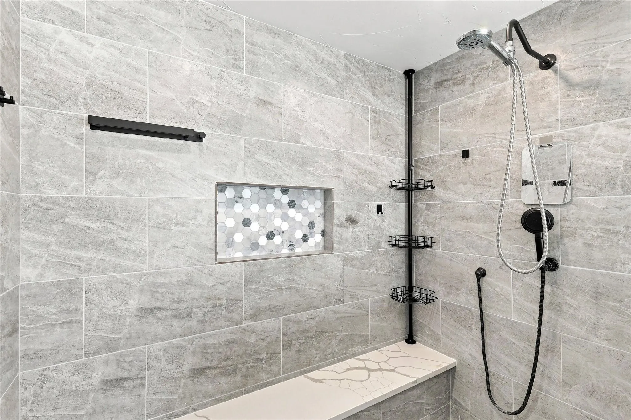 Tiled shower with a built-in niche featuring mosaic hexagon tiles, a quartz-finish bench, and a modern shower system