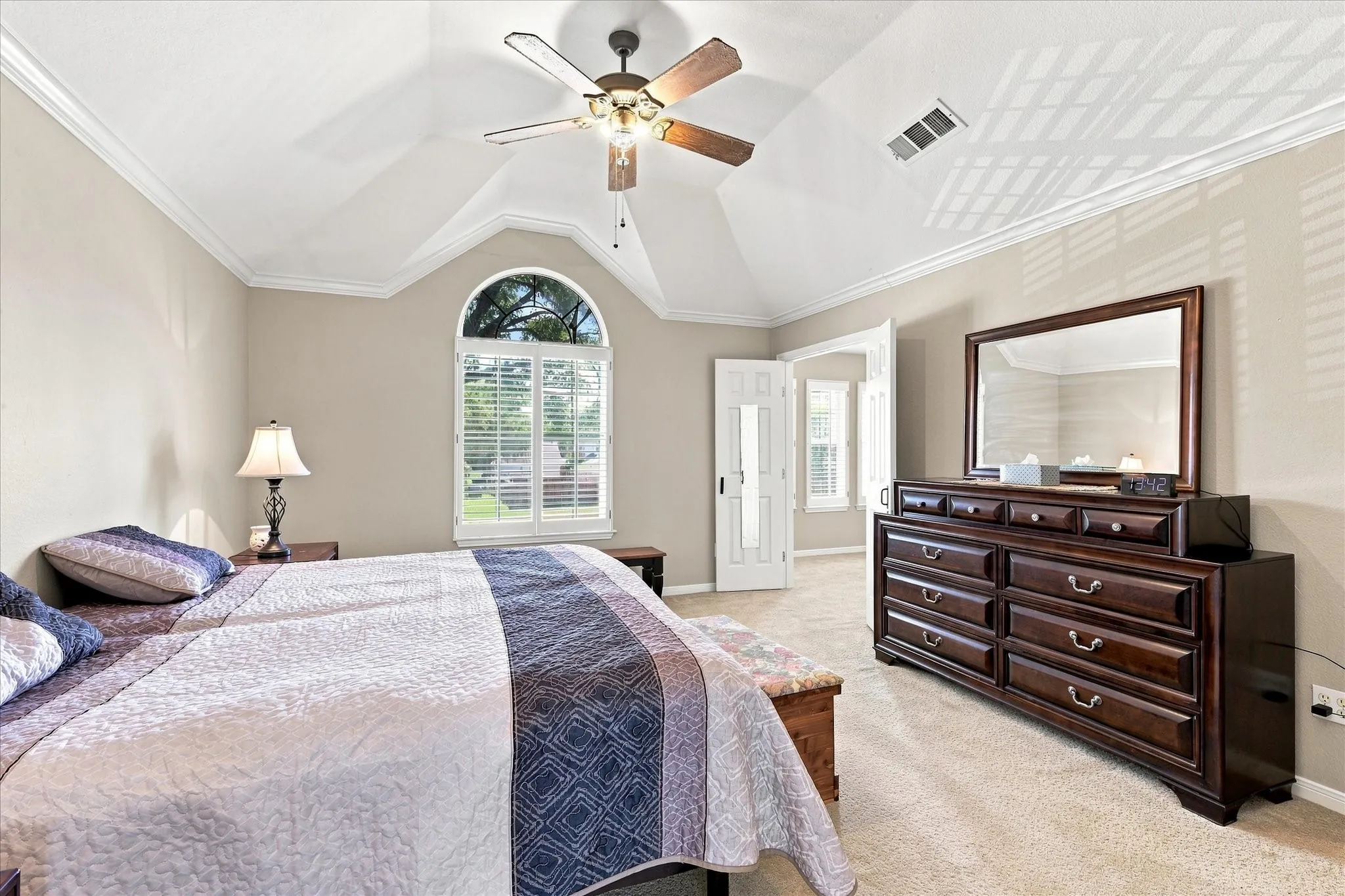 Vaulted ceiling, crown molding, arched window with plantation shutters, ceiling fan, and carpet flooring