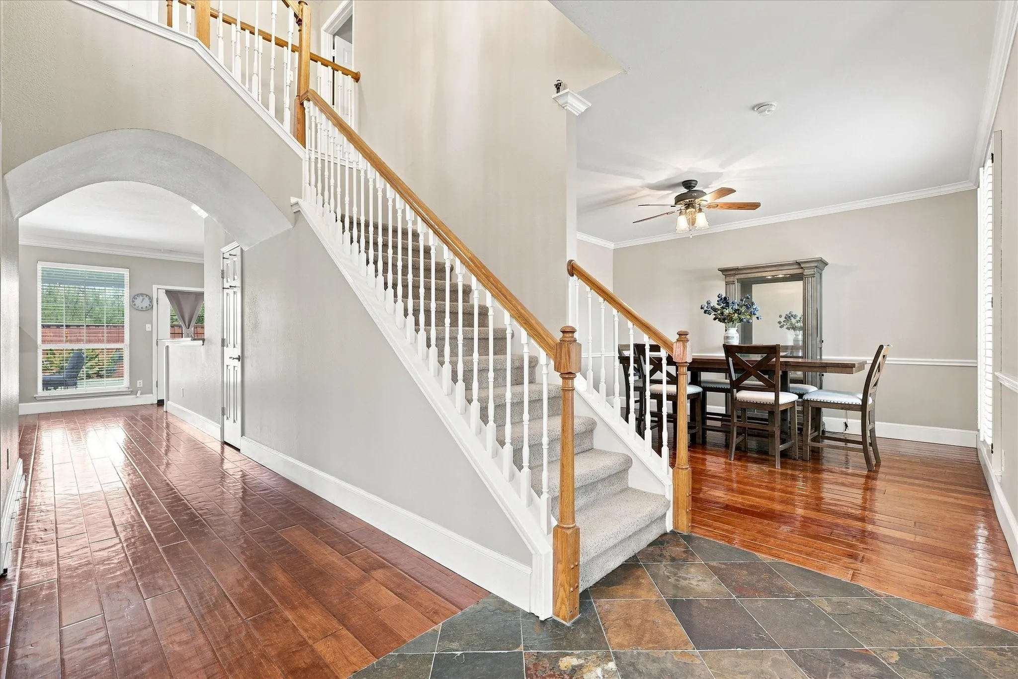 Hardwood flooring, slate tile entry, carpeted staircase with white balusters and wood handrails, and an arched hallway opening