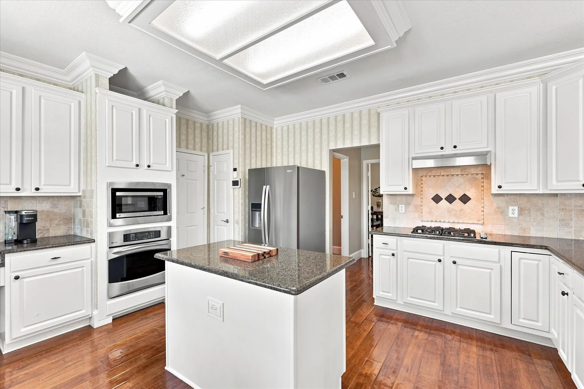 White cabinetry with crown molding, stainless steel appliances, central island, wood-finish flooring, and a gas cooktop with tile backsplash