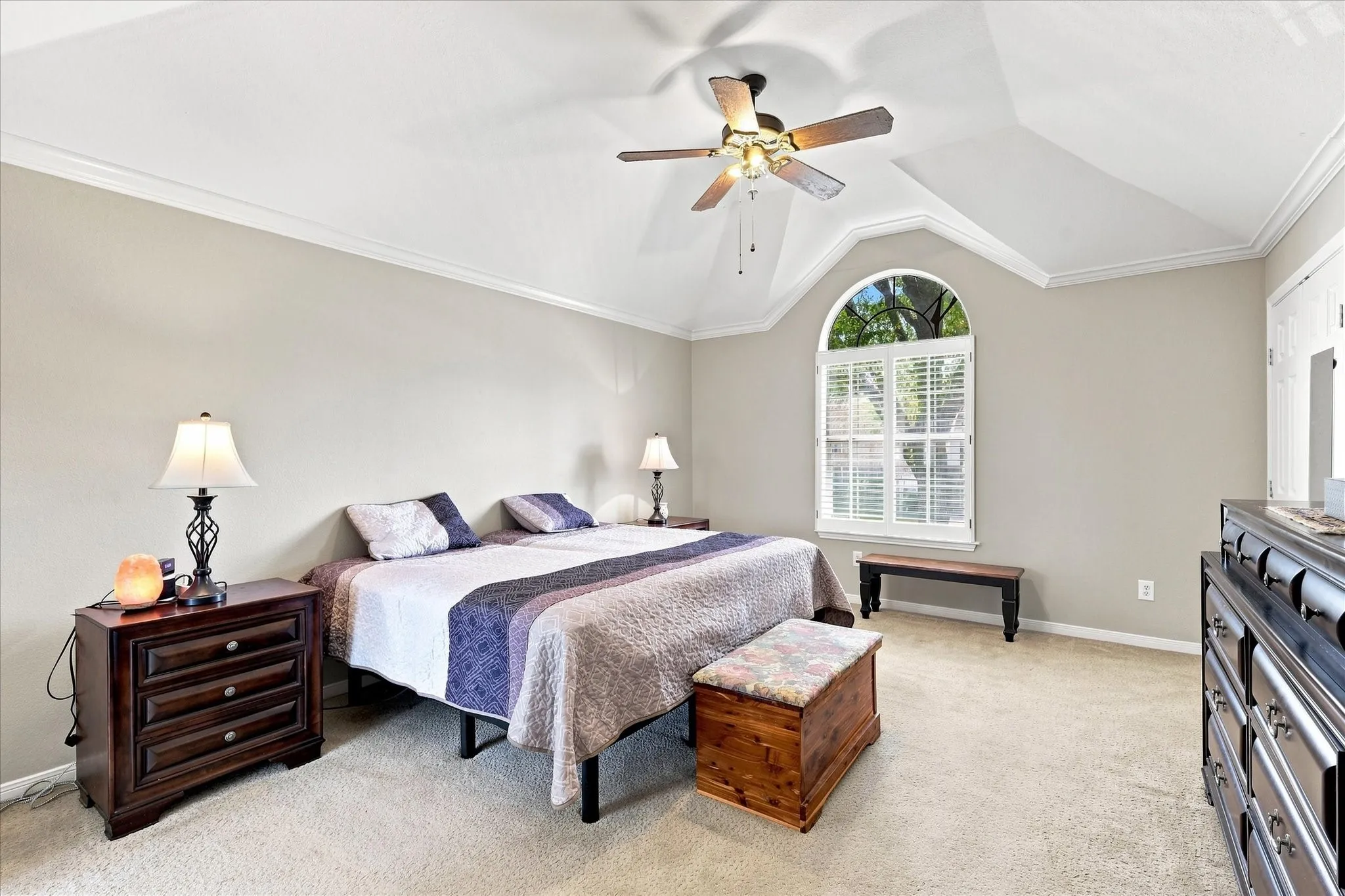 Vaulted ceiling with crown molding, ceiling fan, arched window, and carpeted flooring