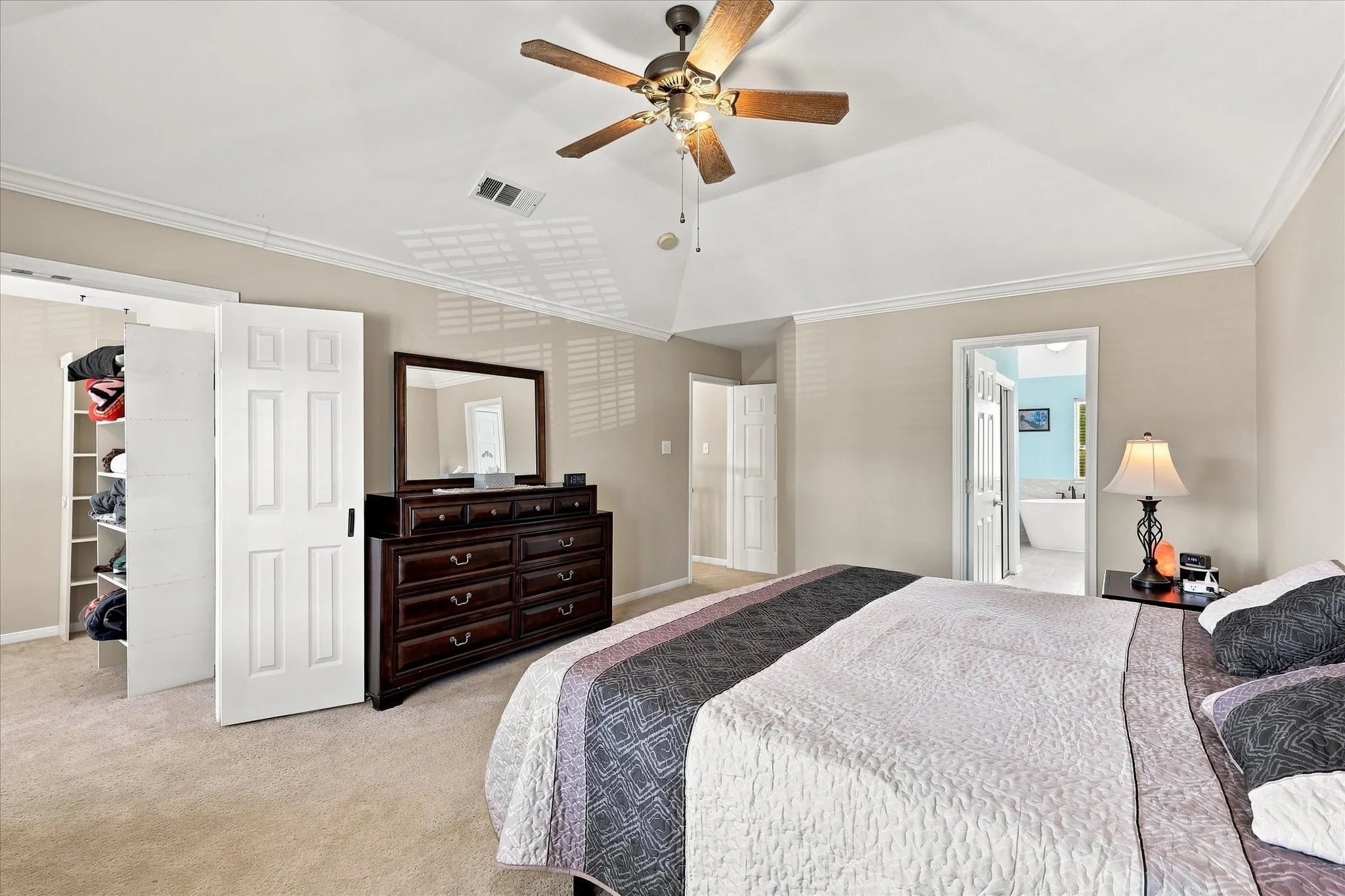 Vaulted ceiling with crown molding, ceiling fan with light fixture, carpeted flooring, and built-in closet shelving