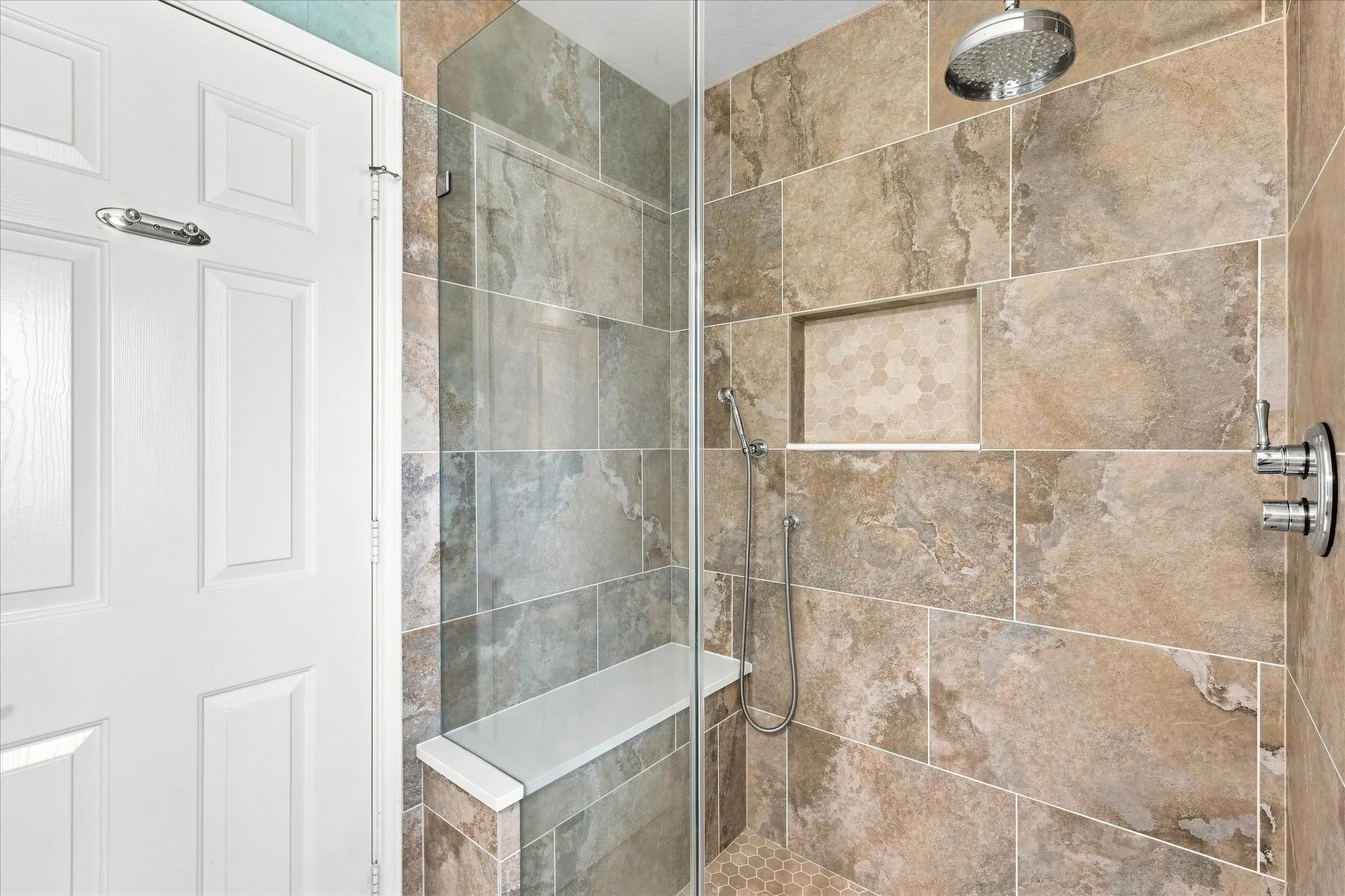 Walk-in shower with clear glass enclosure, a built-in bench, recessed niche with hexagonal tile, handheld shower, and a rain shower head