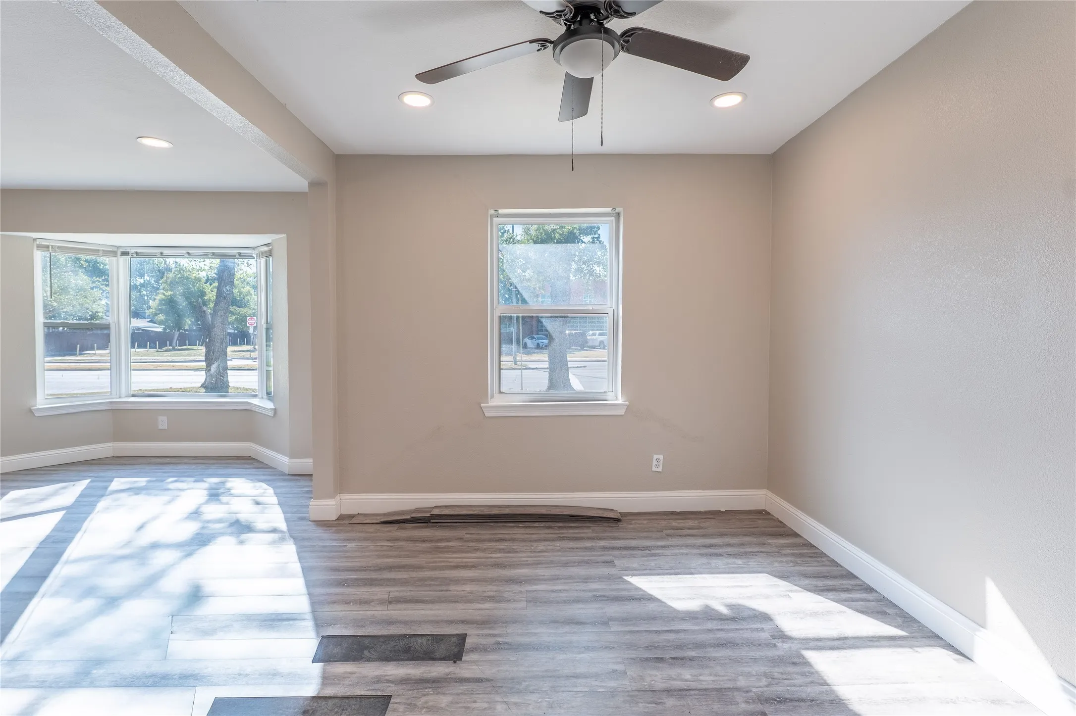 Wood-finish flooring, bay window, recessed lighting, ceiling fan, and neutral wall tones