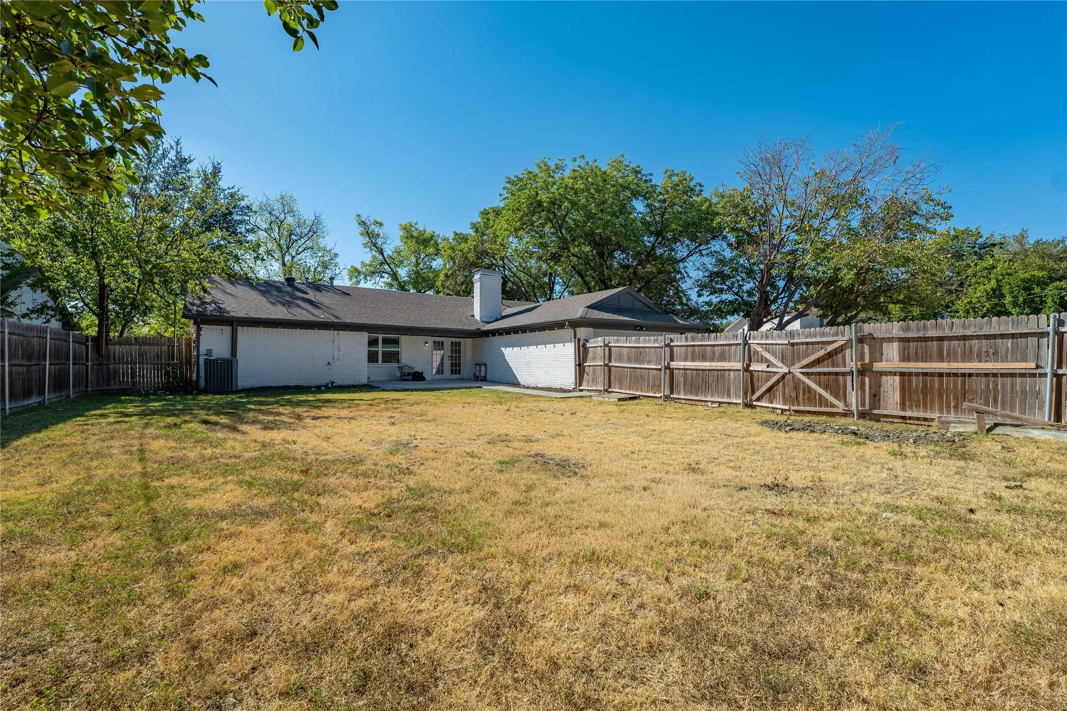 Expansive rear yard featuring a wood privacy fence, concrete patio, and mature trees