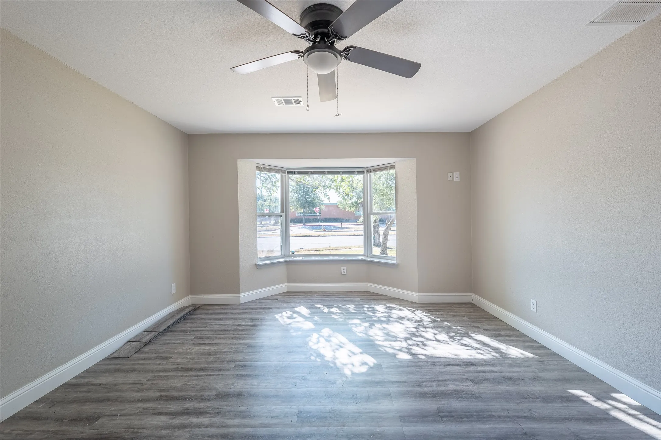 Bay window, ceiling fan, wood-finish flooring, neutral wall tones, white trim