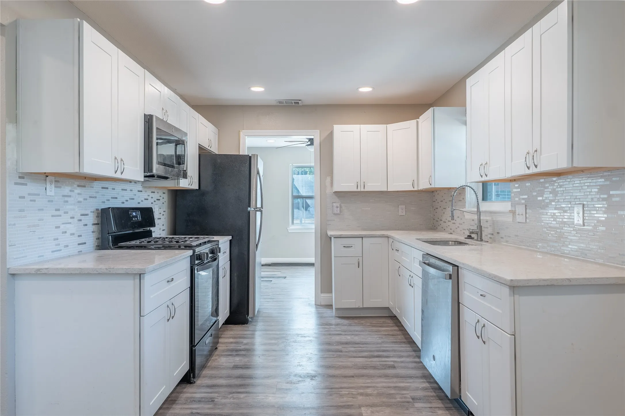 Kitchen featuring white shaker-style cabinetry, light-toned countertops, a mosaic tile backsplash, wood-finish flooring, and recessed lighting