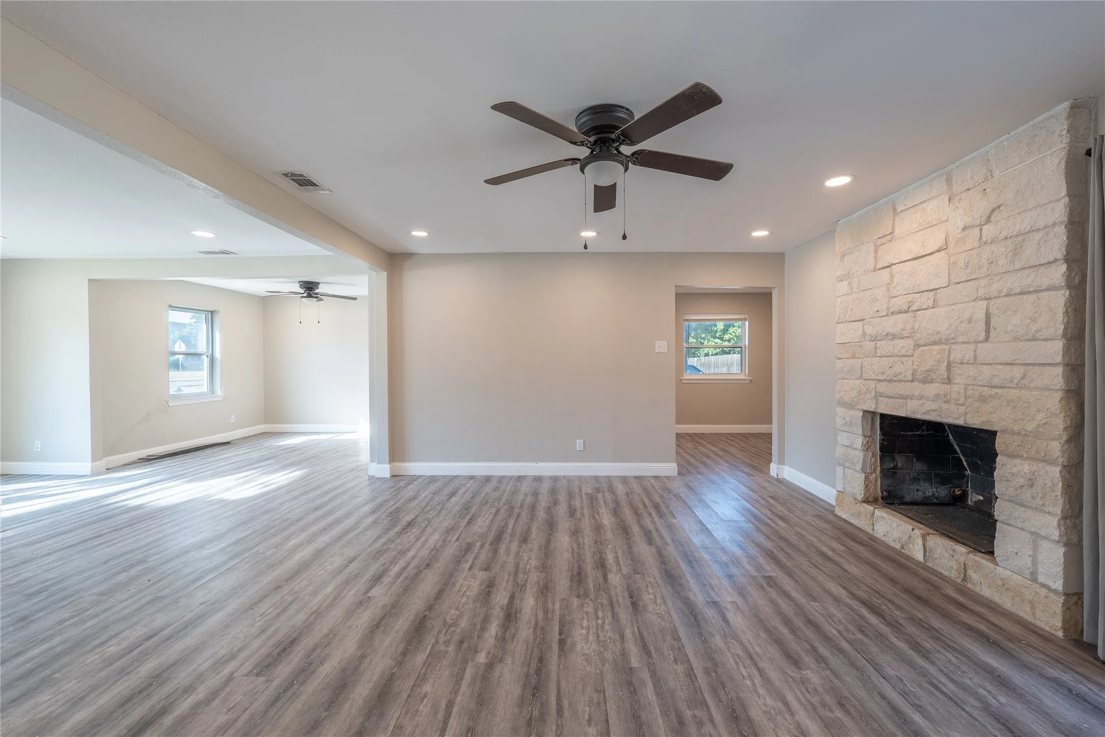 Spacious living area featuring wood-finish flooring, recessed lighting, and a stone-clad fireplace