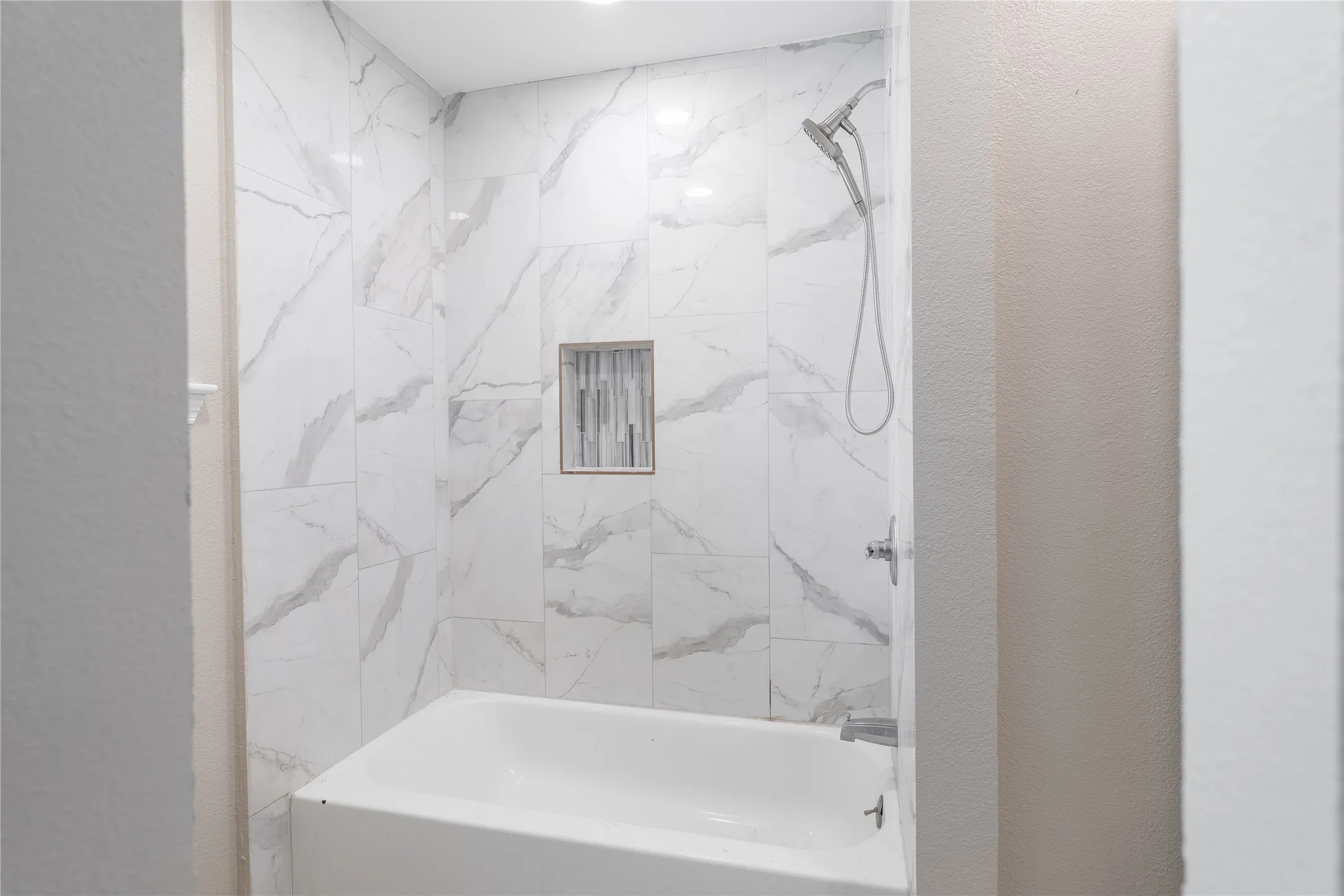 Bathtub with a tiled surround featuring a built-in niche, complete with a showerhead and faucet