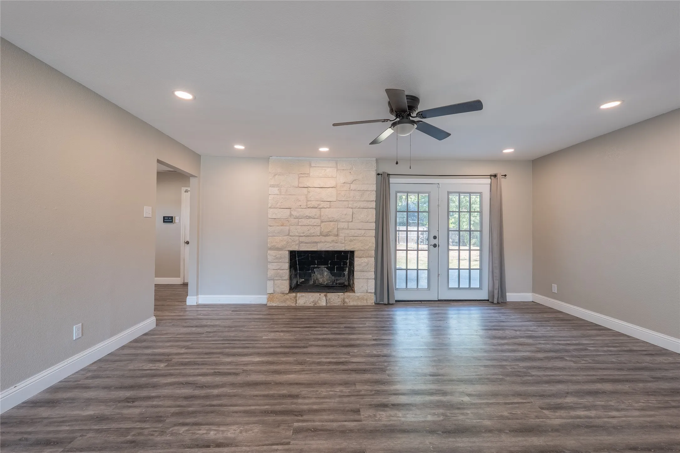 Stone-clad fireplace with a dark firebox, wood-finish flooring, recessed lighting, and a ceiling fan