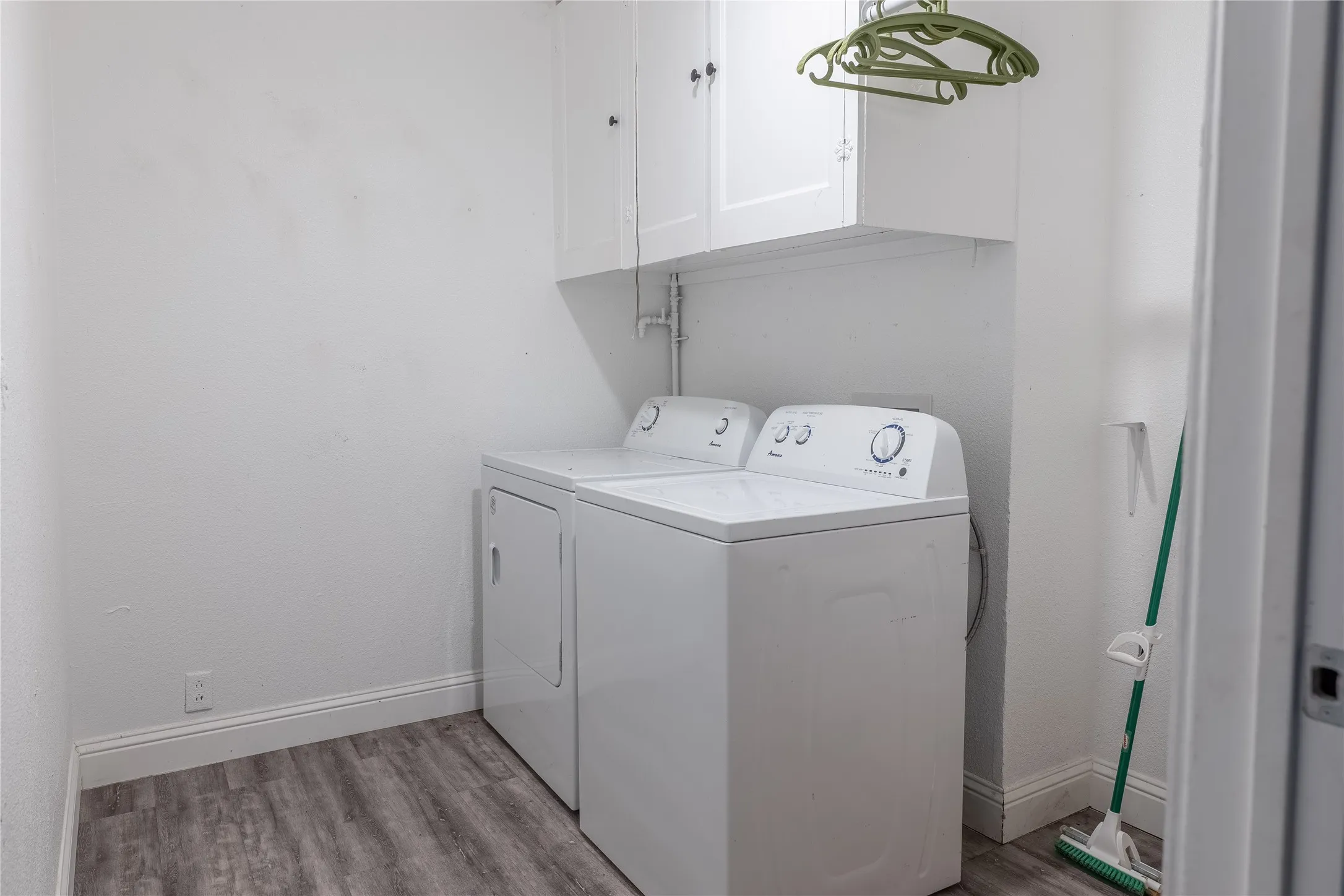 Laundry area featuring wood-finish flooring, white cabinetry, and a utility shelf