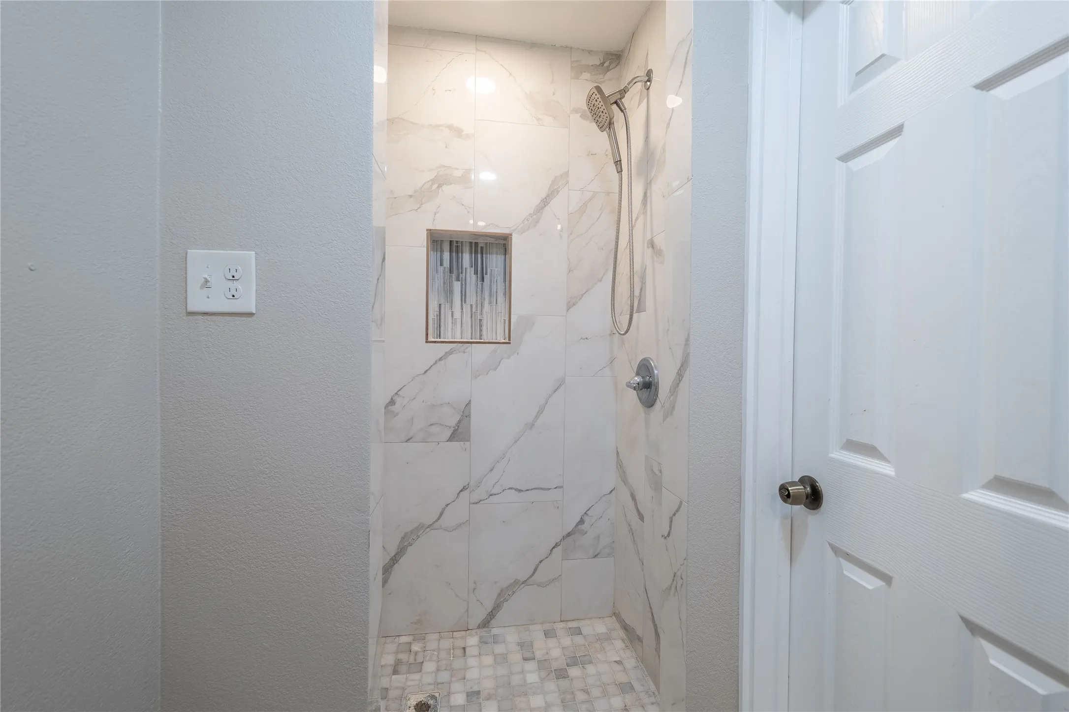 Walk-in shower with large-format tile walls, mosaic tile flooring, a built-in shower niche, and a brushed nickel shower head
