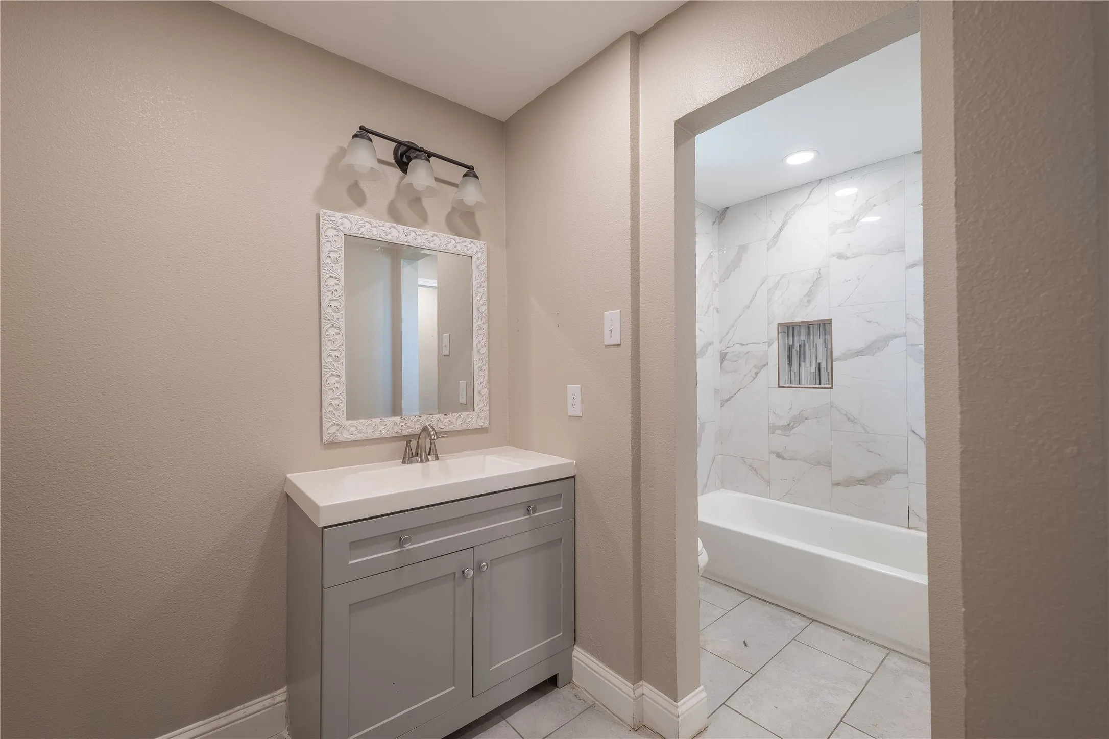 Bathroom vanity with a white countertop and a framed mirror, complemented by a three-light fixture