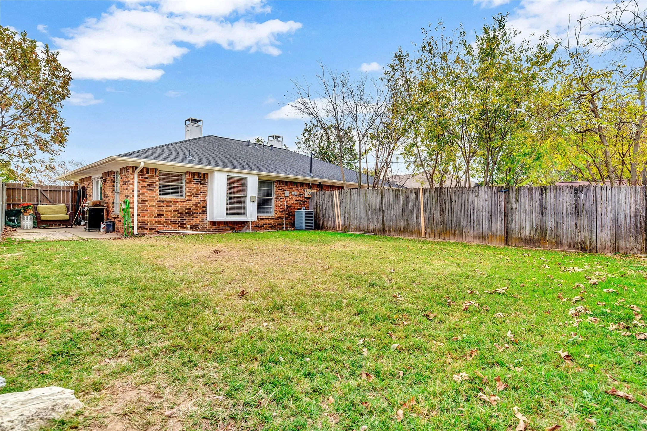Expansive backyard featuring a brick exterior, covered patio, and a wood privacy fence