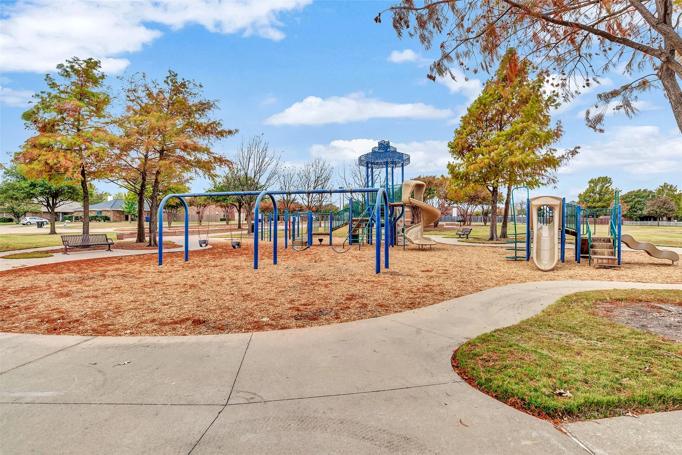 Community park featuring a playground with slides and swings, multiple benches, and mature trees