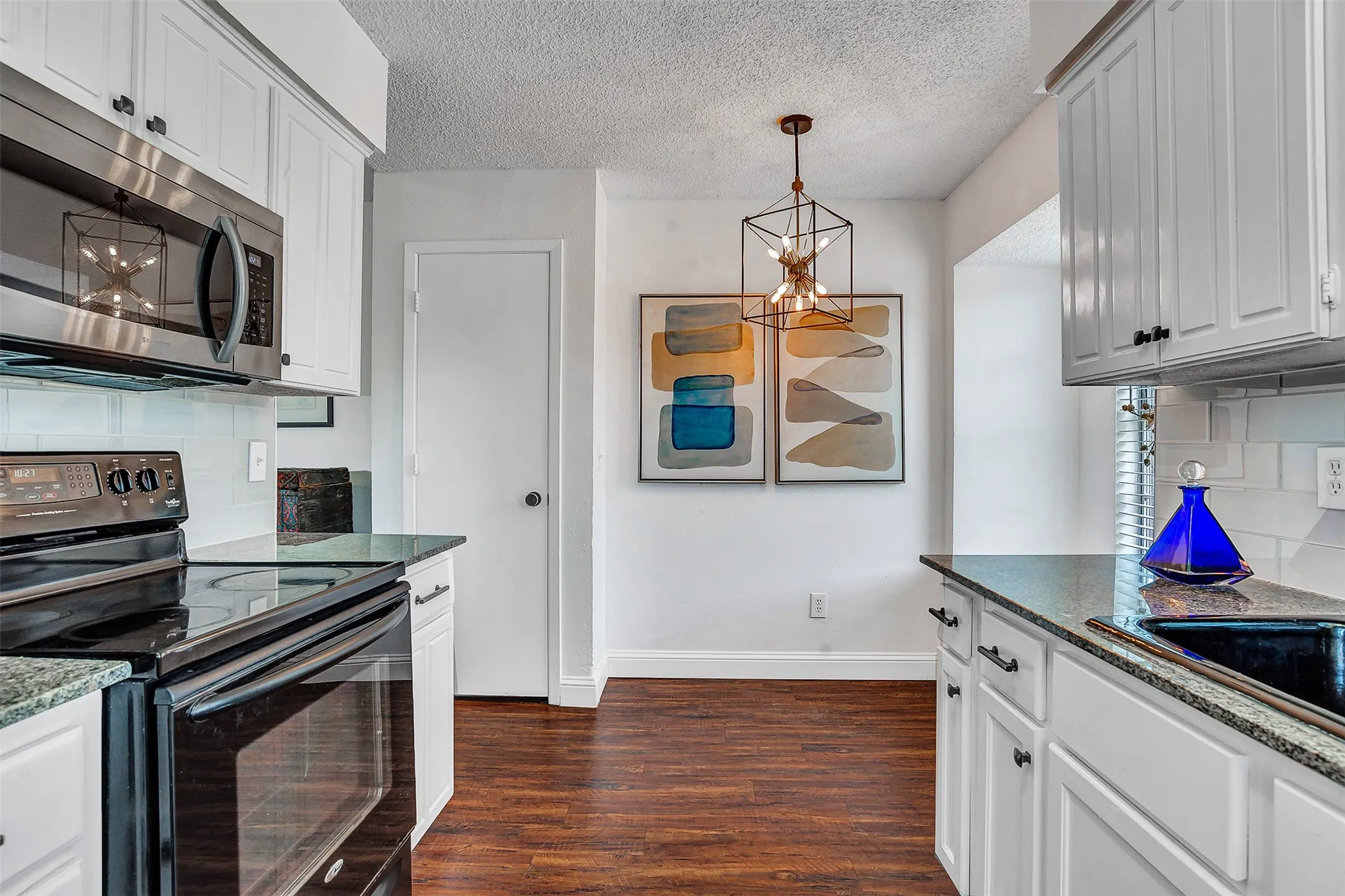 Kitchen featuring wood-finish flooring, white cabinetry, dark countertops, a stainless steel microwave, and a black range