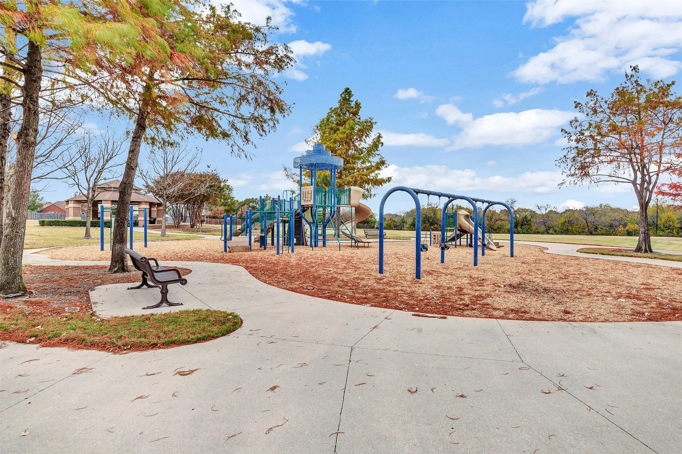 Community park featuring a playground, swings, paved walking paths, and mature trees