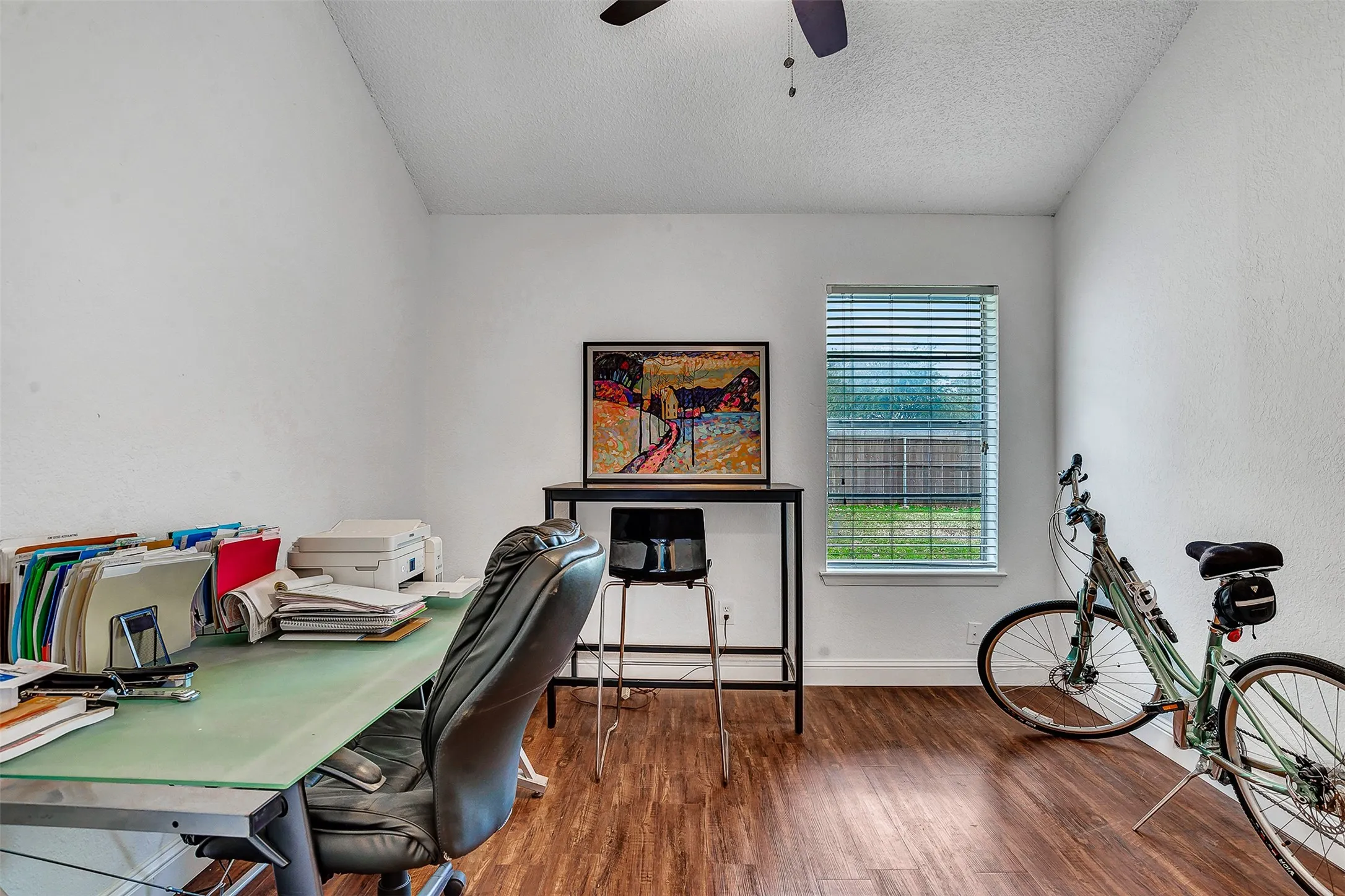 Vaulted ceiling, wood-finish flooring, rectangular window with blinds, and ceiling fan