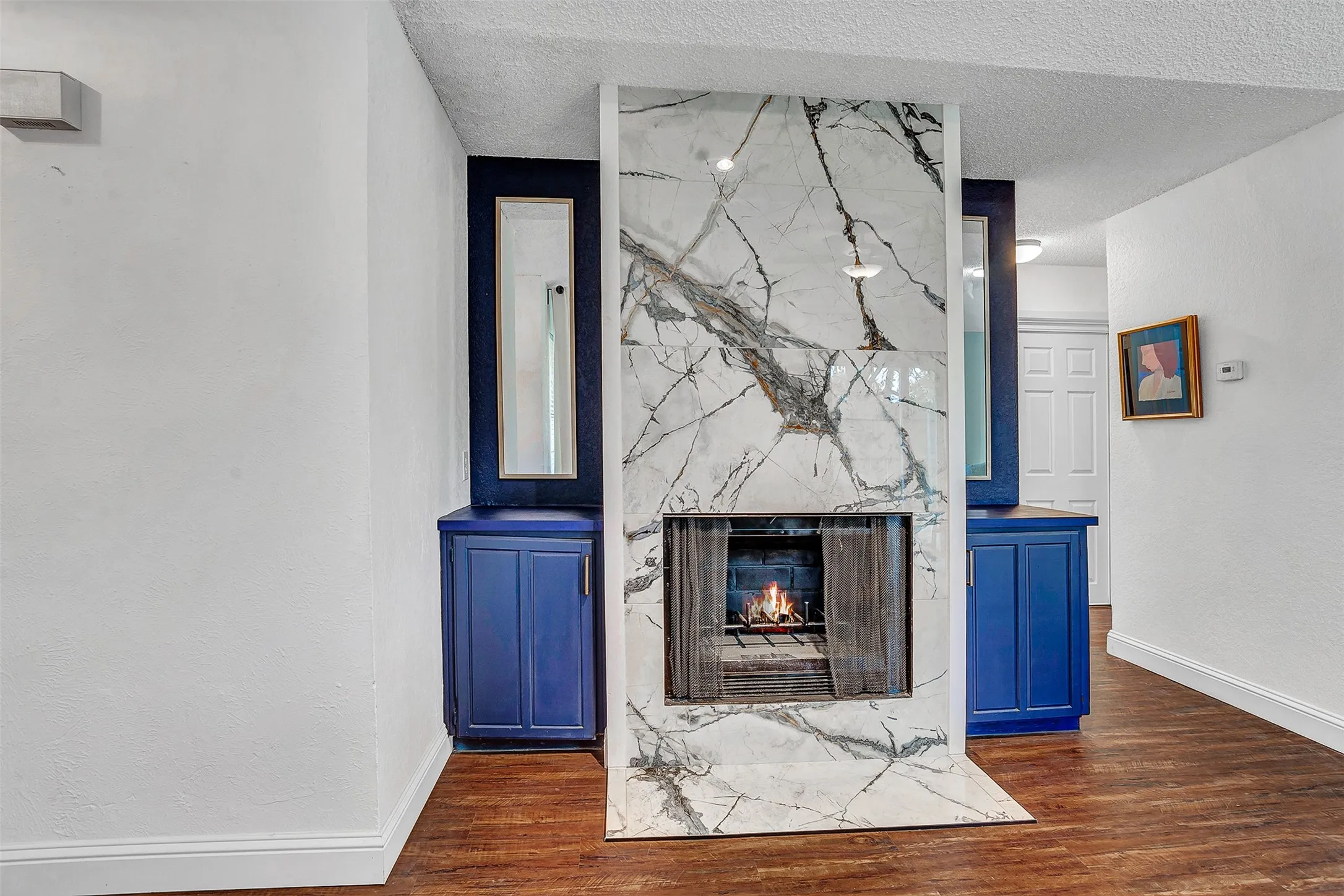 Central fireplace featuring a marble surround, wood-finish flooring, and built-in cabinetry with integrated mirrors