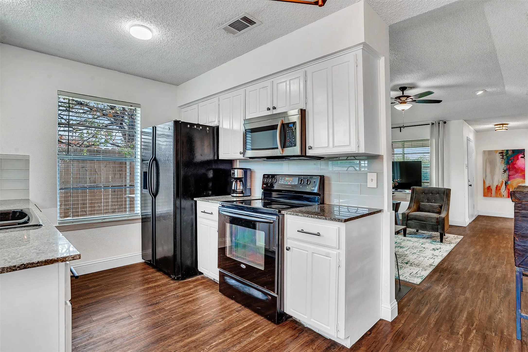 Kitchen with white cabinetry, stainless steel microwave, black electric range, and wood-finish flooring