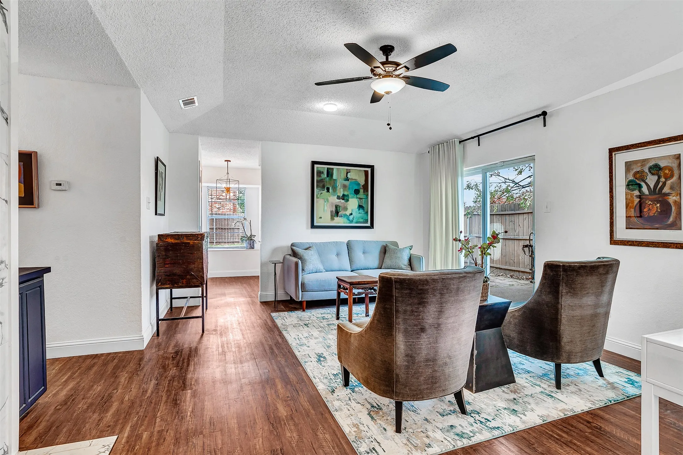 Wood-finish flooring throughout, ceiling fan with integrated lighting, white walls, and a sliding glass door providing exterior access