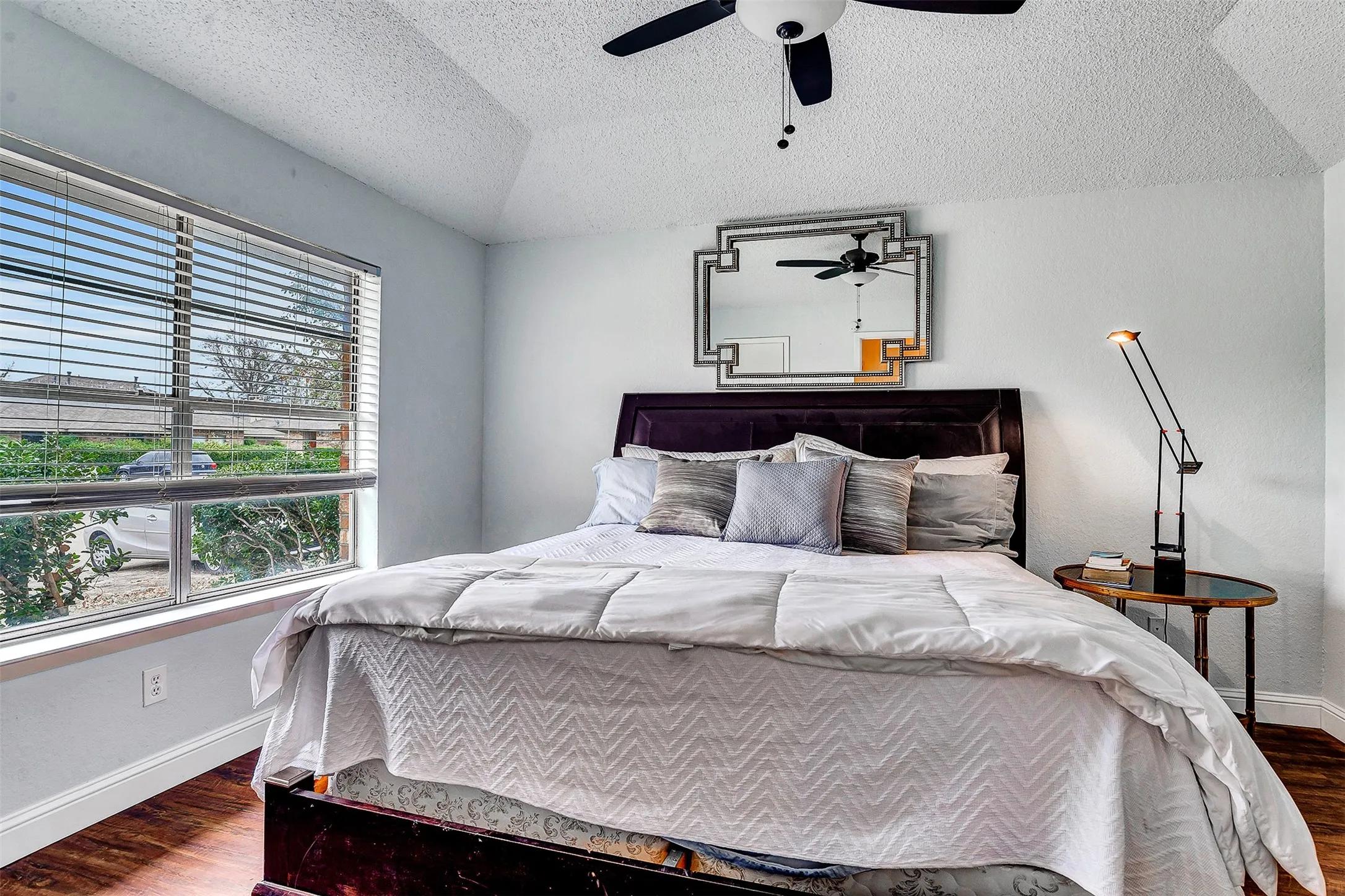 Vaulted ceiling with a ceiling fan, window with horizontal blinds, wood-finish flooring, and light-toned walls