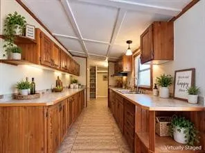Galley kitchen featuring wood cabinetry, light-toned countertops, under-cabinet lighting, and a ceiling-mounted light fixture