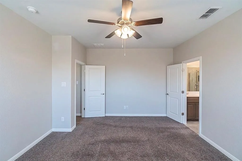 Unfurnished bedroom featuring visible vents, a ceiling fan, carpet flooring, ensuite bath, and baseboards