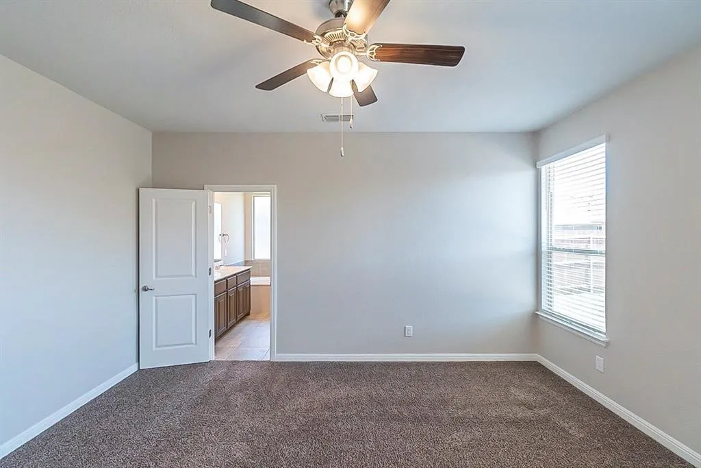 Empty room featuring light carpet, baseboards, visible vents, and a ceiling fan