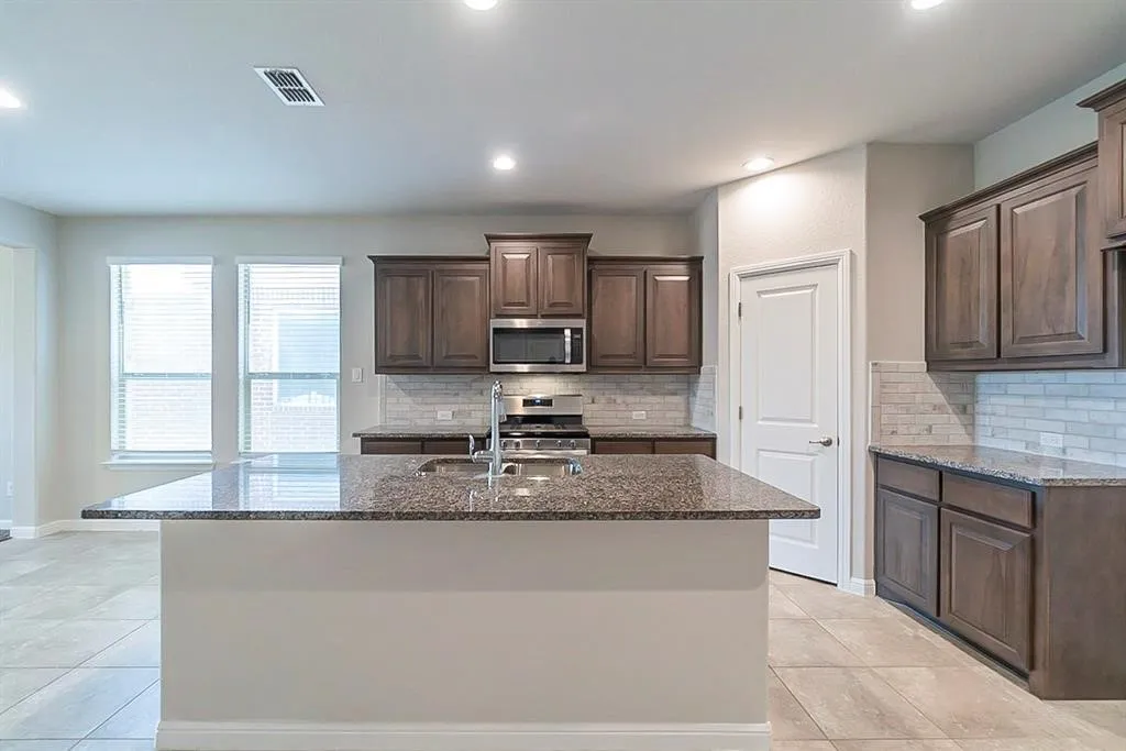 Kitchen with visible vents, appliances with stainless steel finishes, dark stone countertops, a sink, and light tile patterned flooring