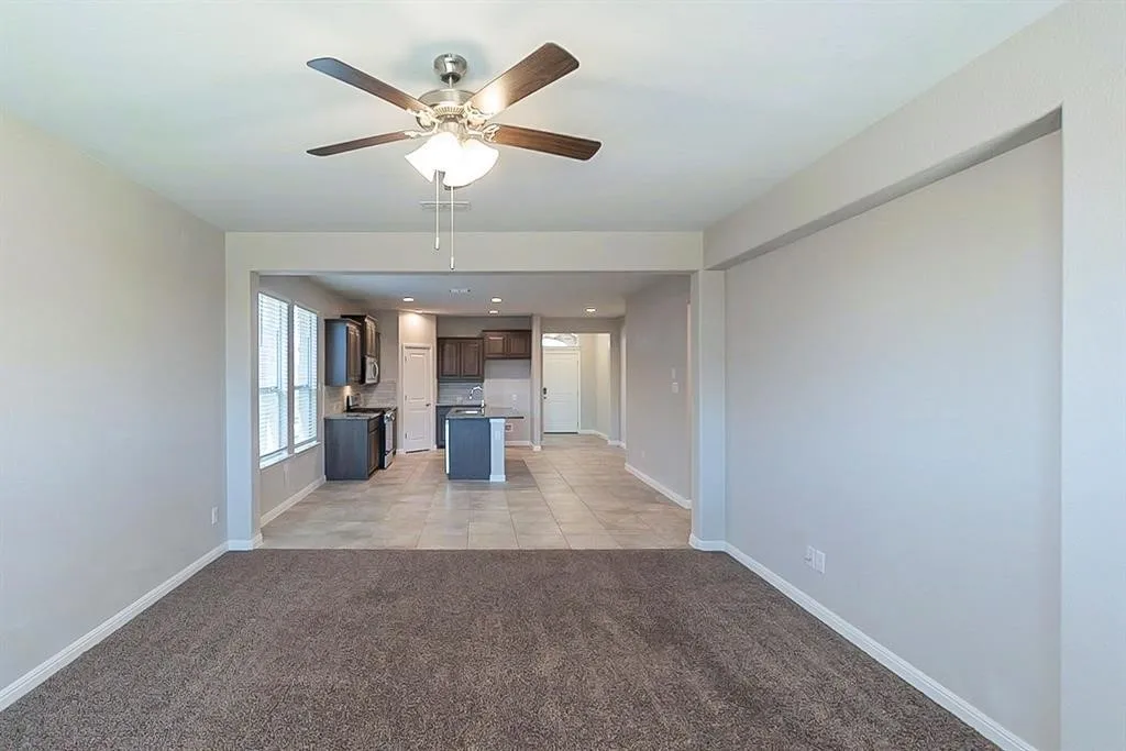 Unfurnished living room with light carpet, ceiling fan, baseboards, and light tile patterned flooring