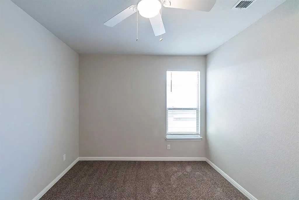 Carpeted spare room featuring visible vents, ceiling fan, and baseboards