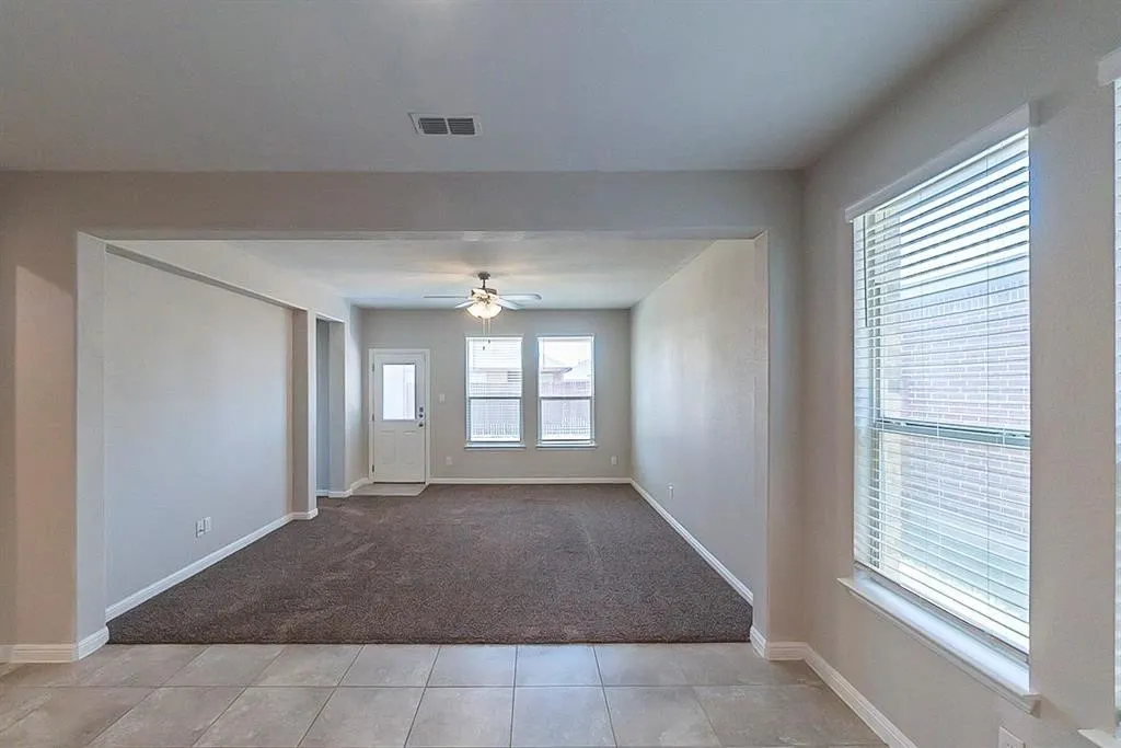 Empty room featuring light tile patterned floors, light carpet, visible vents, baseboards, and a ceiling fan
