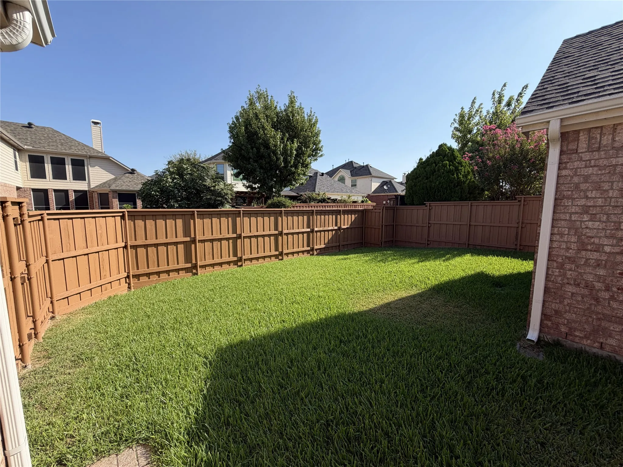 Expansive backyard featuring a manicured lawn, full perimeter privacy fencing, and brick exterior