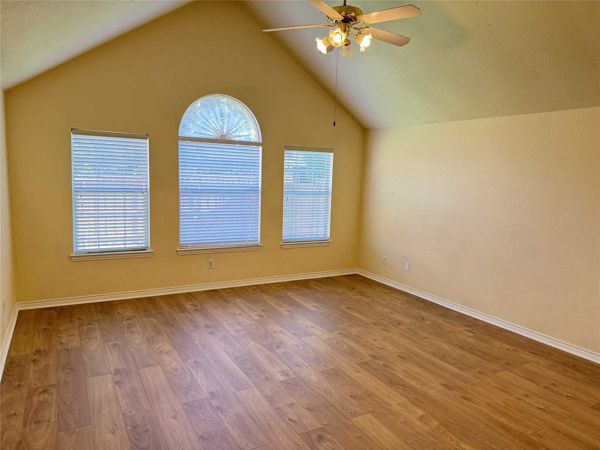 Vaulted ceiling with a ceiling fan light fixture, wood-finish flooring, and multiple windows including an arched window