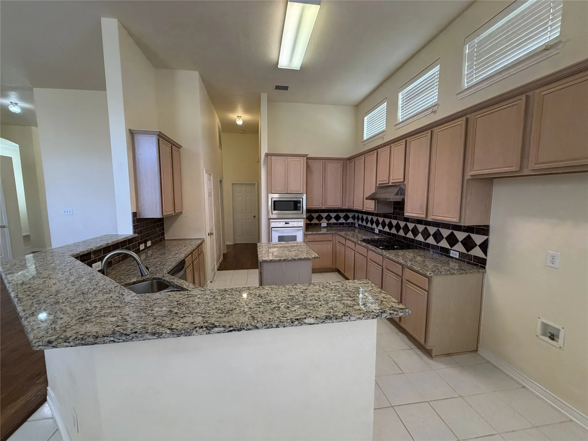 Kitchen featuring extensive light wood cabinetry, granite countertops, tile flooring, and a patterned tile backsplash