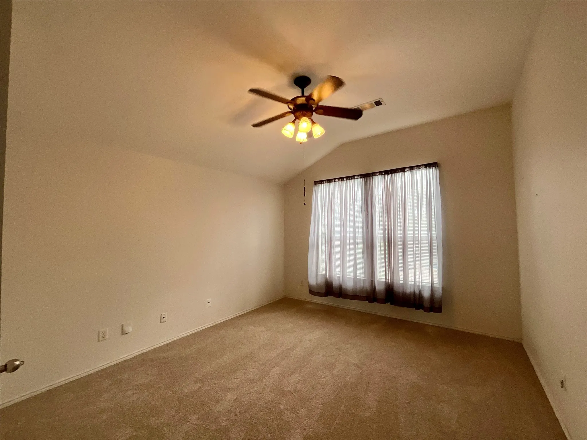 Vaulted ceiling with a ceiling fan light fixture, wall-to-wall carpeting, and a window with sheer and blackout curtains