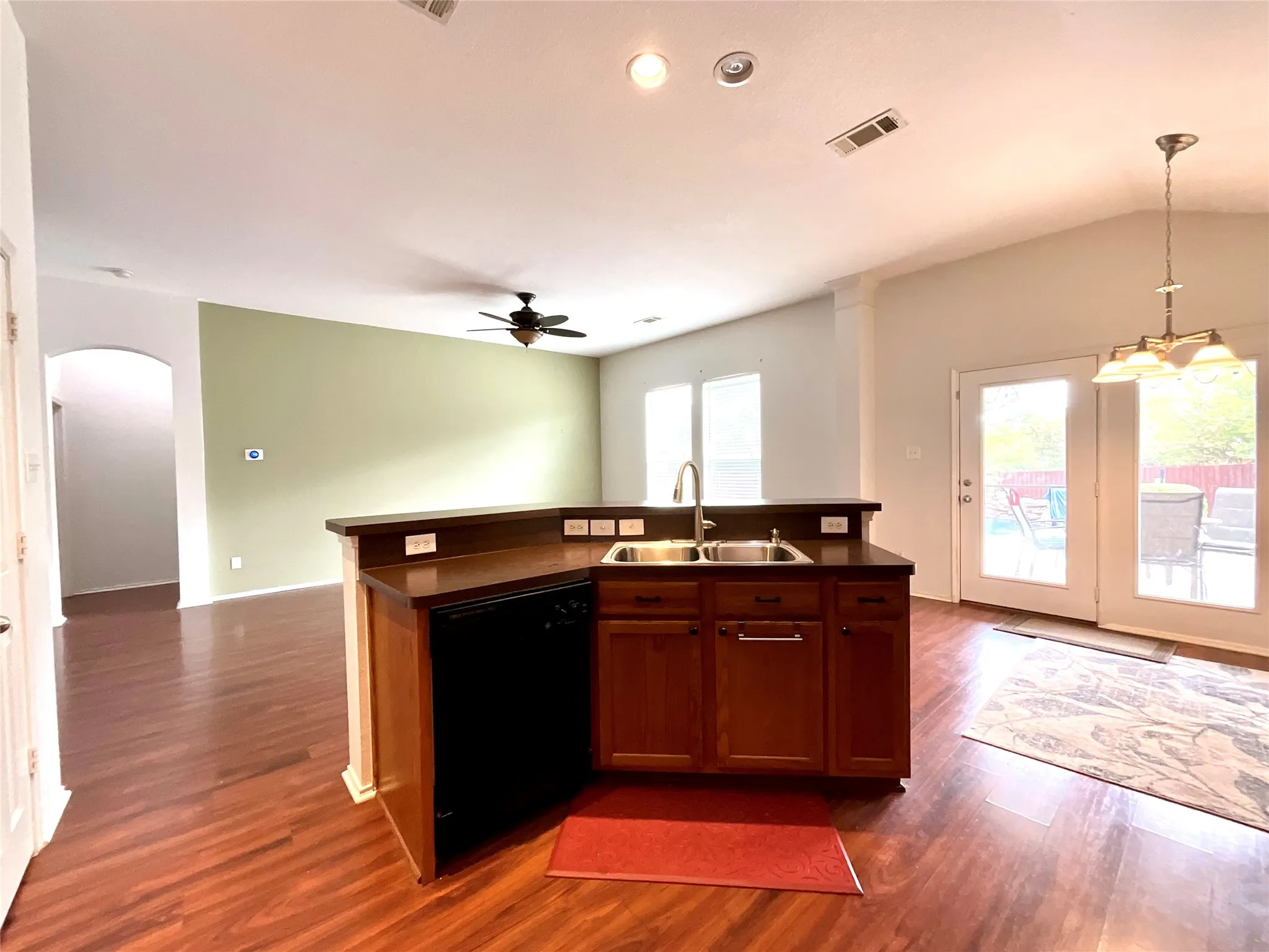 Kitchen island with integrated sink and dishwasher, wood-finish flooring, vaulted ceiling with chandelier, ceiling fan, and French doors providing exterior access