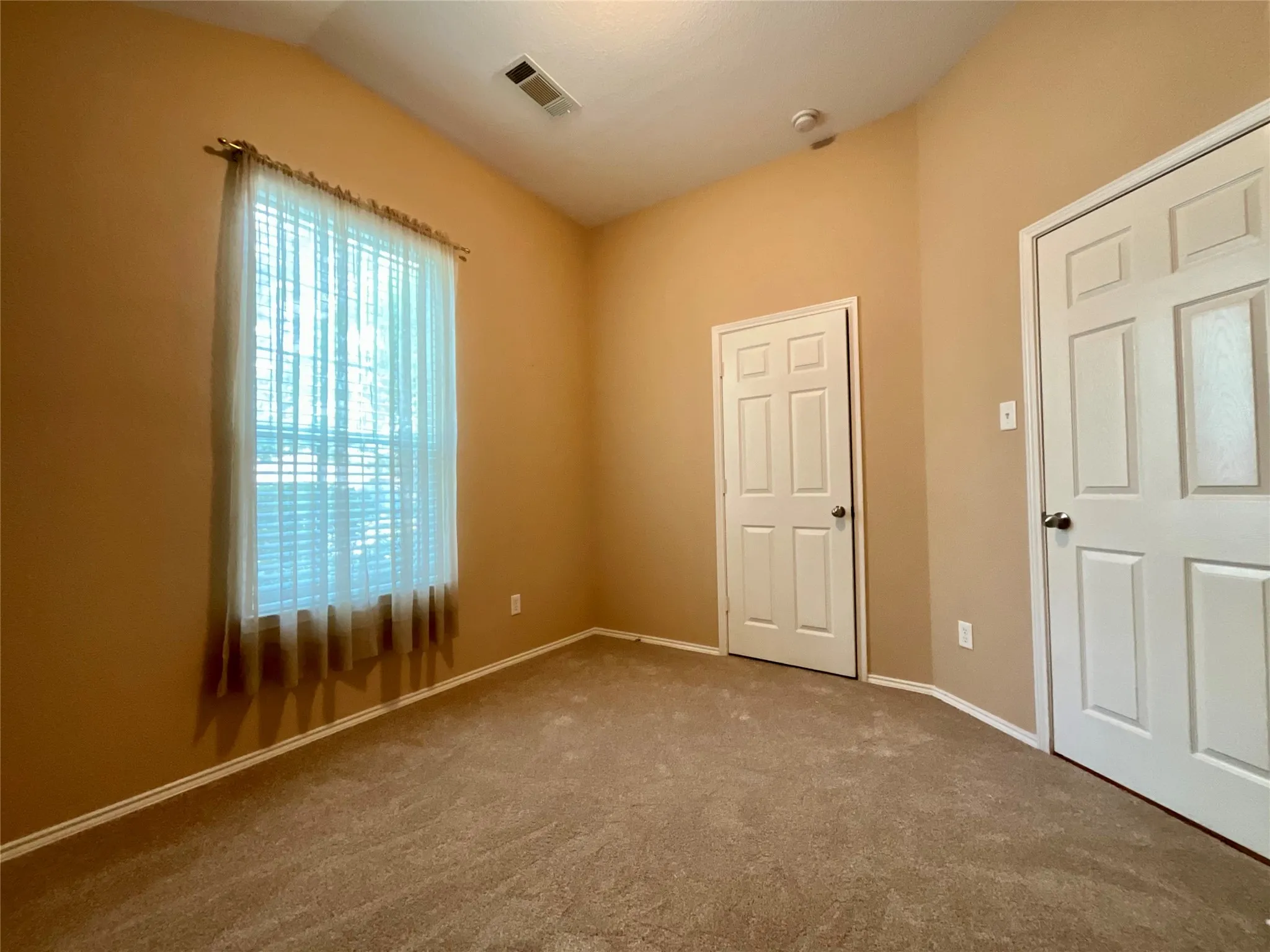 Vaulted ceiling, window with blinds, panel doors, and neutral carpeting