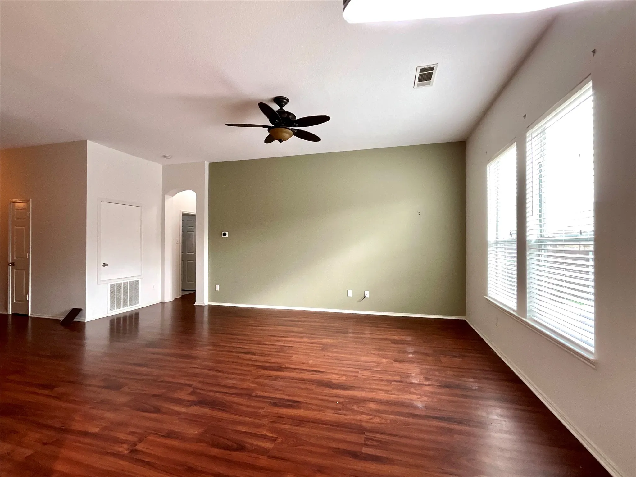 Wood-finish flooring, accent wall, ceiling fan, multiple windows, and an arched doorway