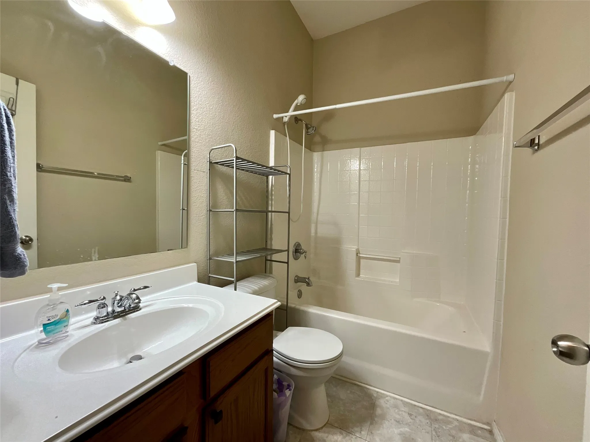 Bathroom featuring a vanity with a white countertop and integrated sink, chrome faucet, wall-mounted mirror, and a shower/tub combination with a white surround